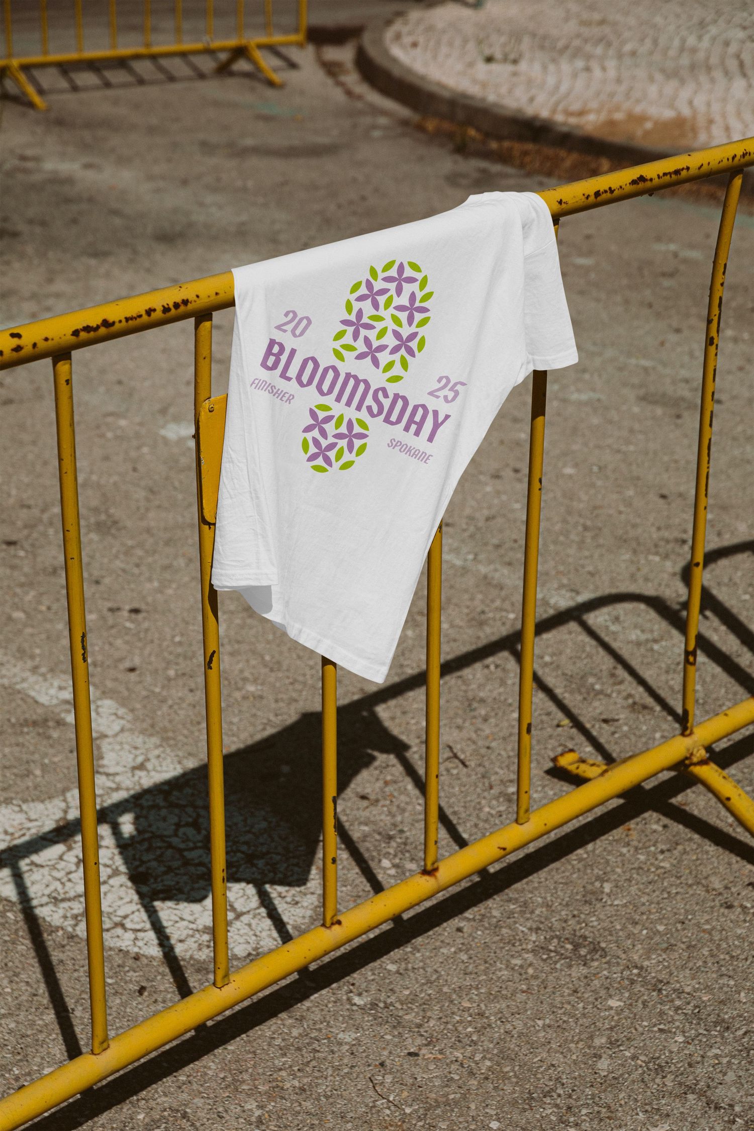 White Bloomsday 2025 event t-shirt draped over yellow metal barrier on sunny pavement.
