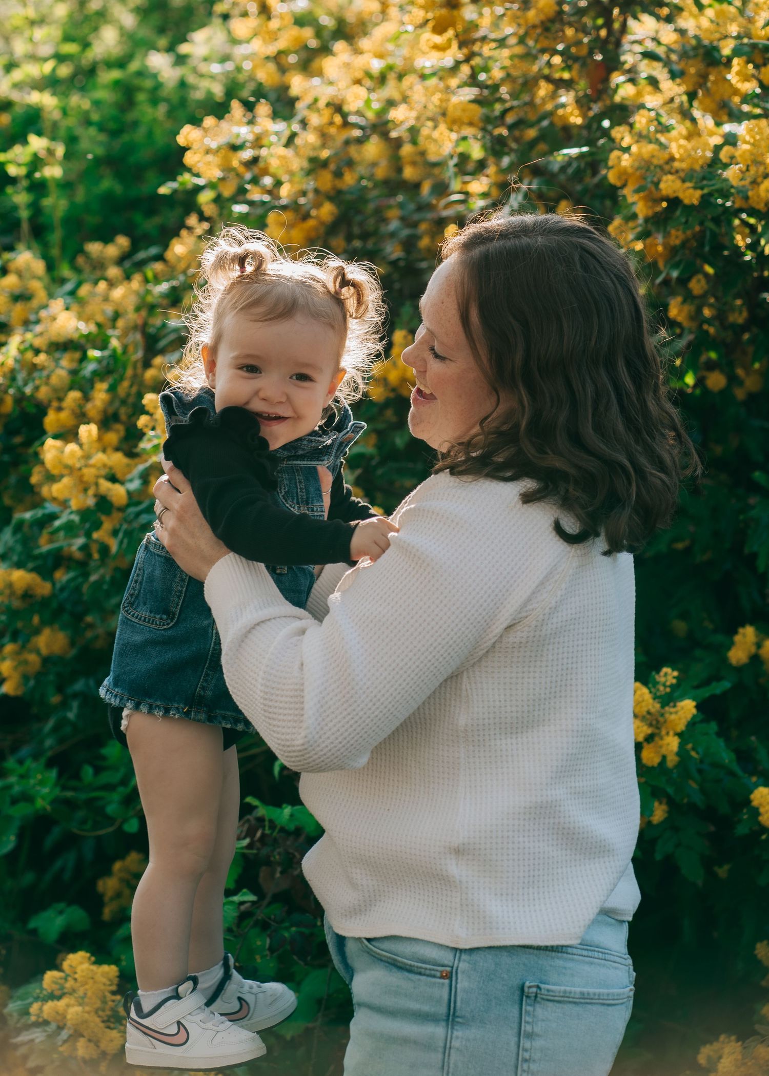 Playful family moments captured against backdrop of yellow flowering bushes in garden.