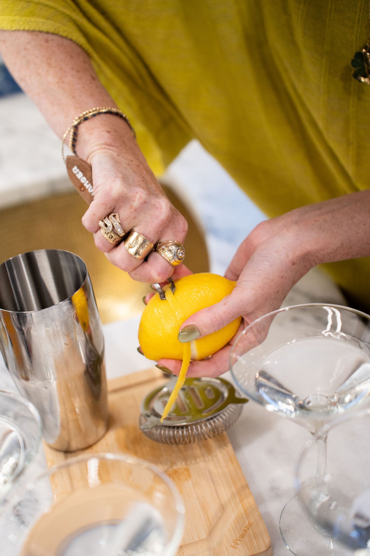 Hands preparing citrus garnishes on a wooden cutting board with bar tools.
