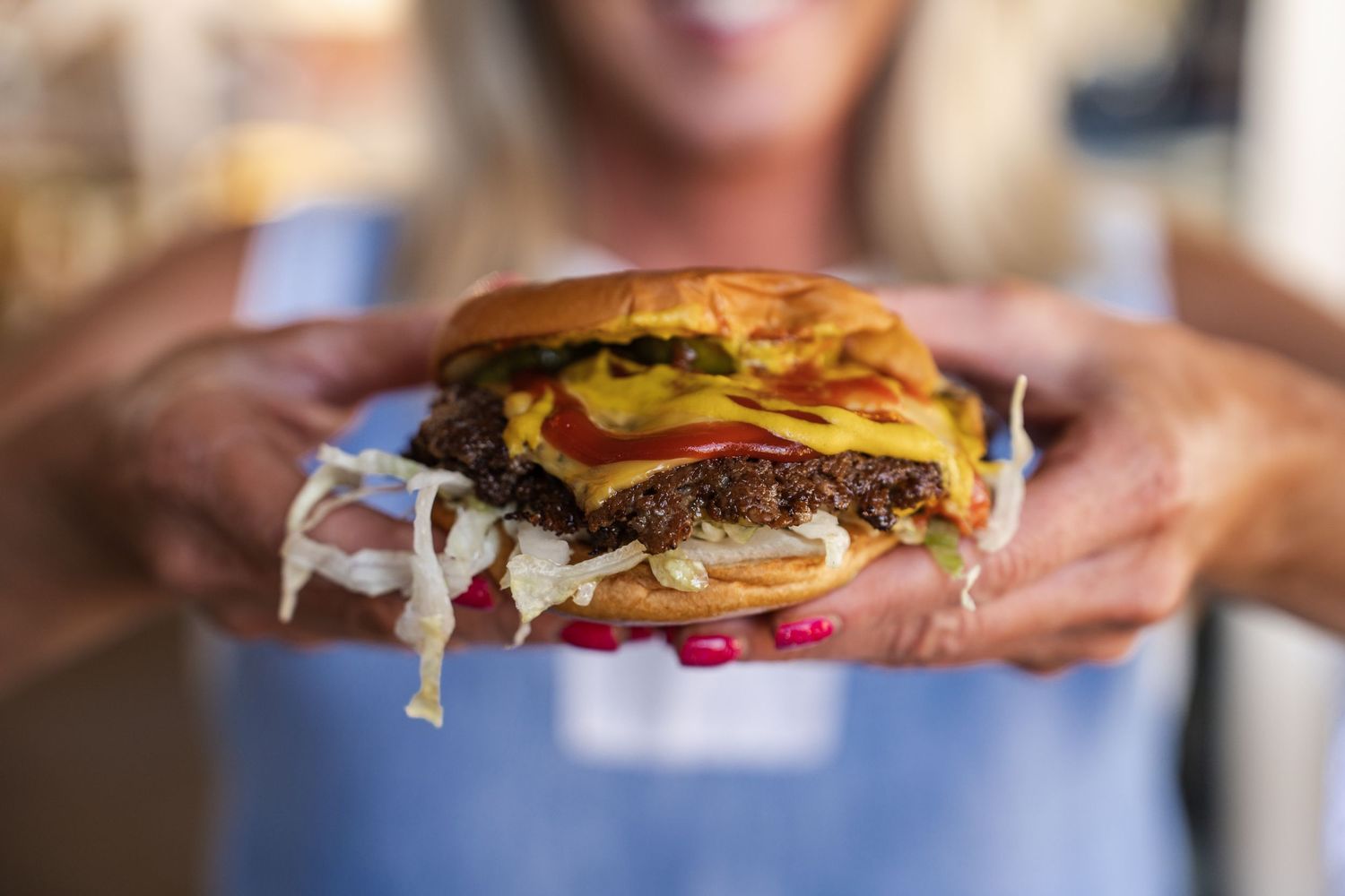 Hands holding colorful gourmet burgers with melted cheese and fresh toppings.