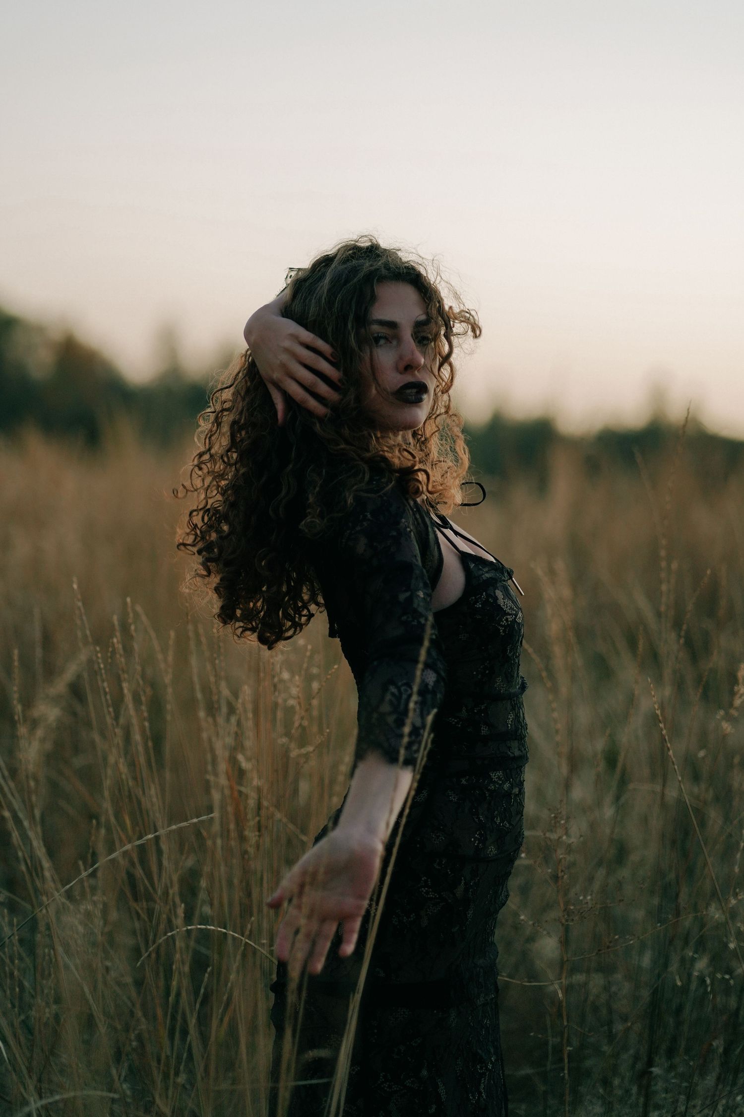Artistic portrait in a field at dusk with natural movement and flowing curls.