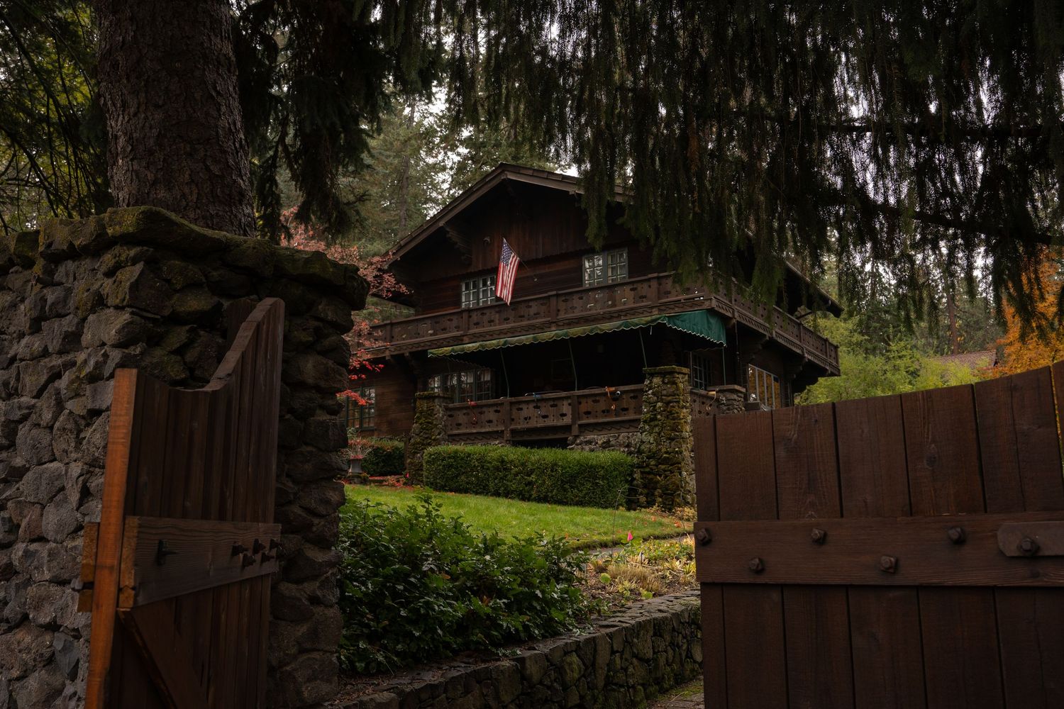 Rustic log cabin with stone foundation viewed through open wooden gates.