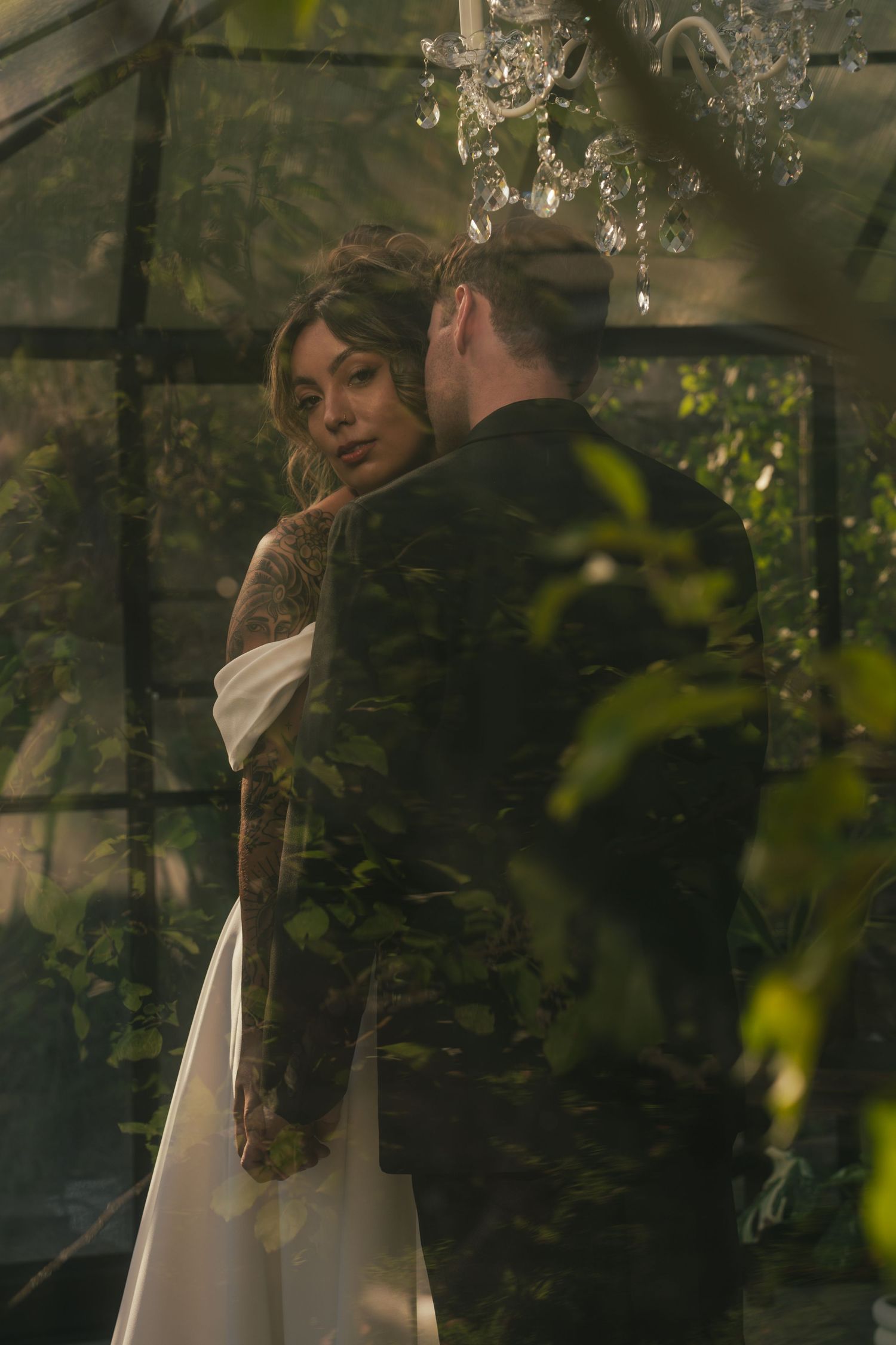 Dreamy wedding scene through glass with chandelier and natural foliage creating atmospheric mood.