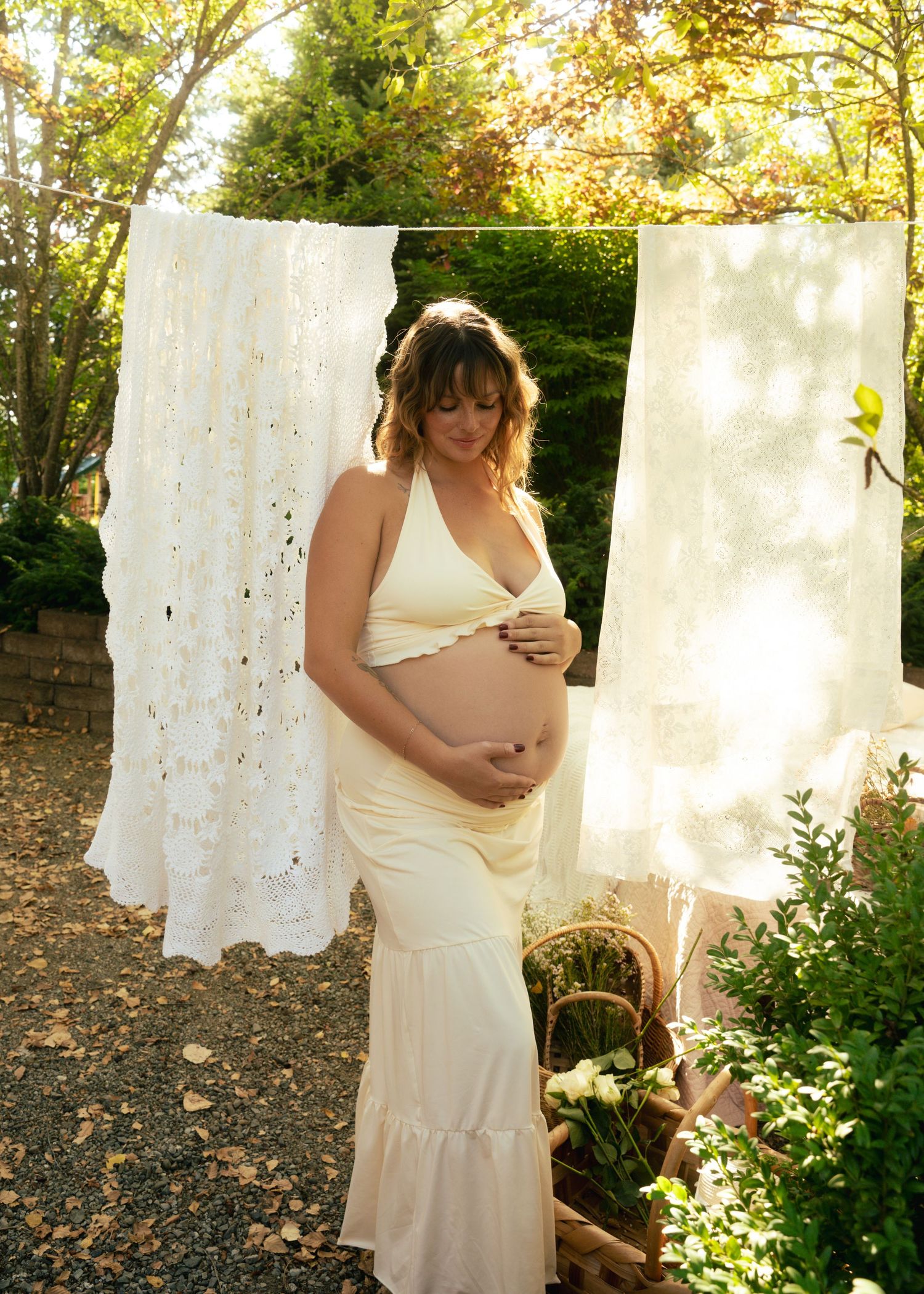Maternity photos in a garden with white linens hanging on a clothesline.