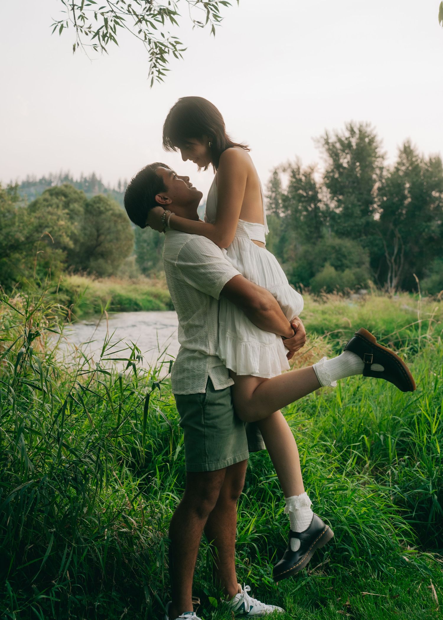 Romantic couple embraces in tall grass by a lake during golden hour photoshoot.