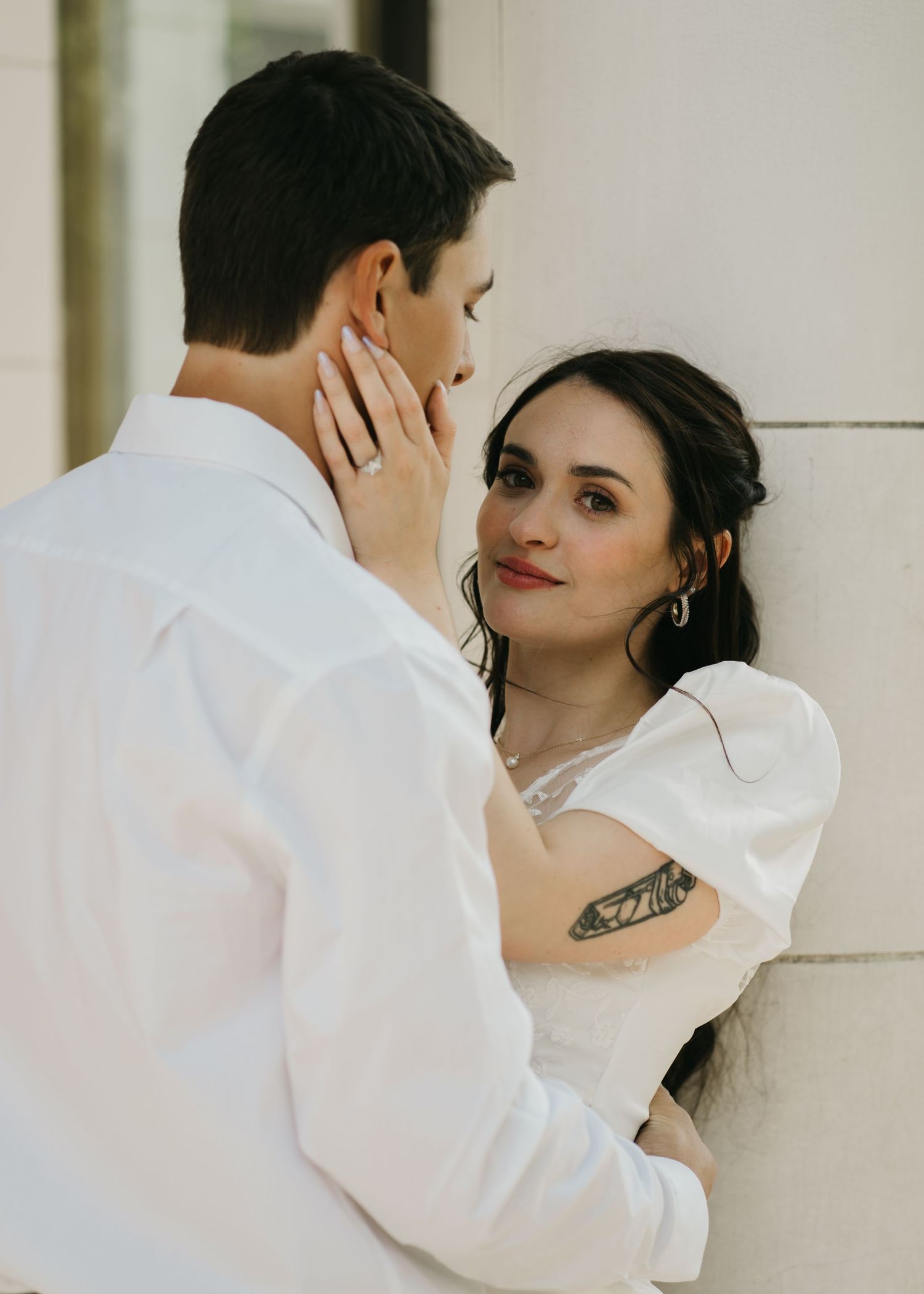 Intimate portrait session against white wall showing delicate details and tattoo art.