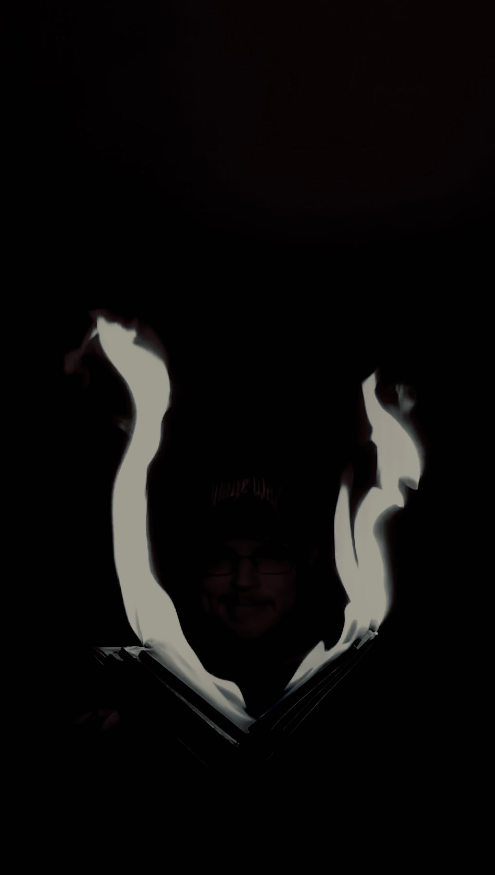 A mysterious figure in darkness illuminated by white flame light from an open book.