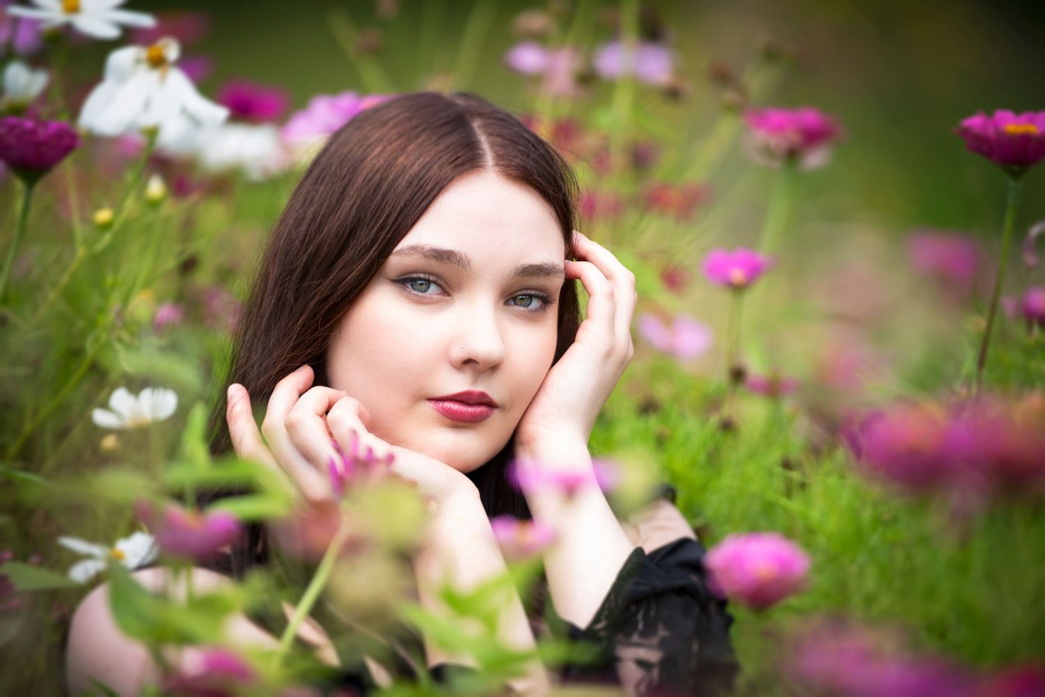 Young woman with blue eyes lying among pink and white cosmos flowers in a garden.