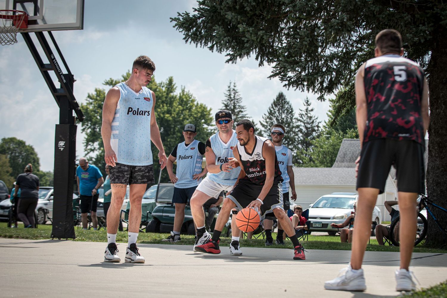 Young men in Polaris jerseys competing in an outdoor Rucker League basketball game on a paved court on a sunny day.