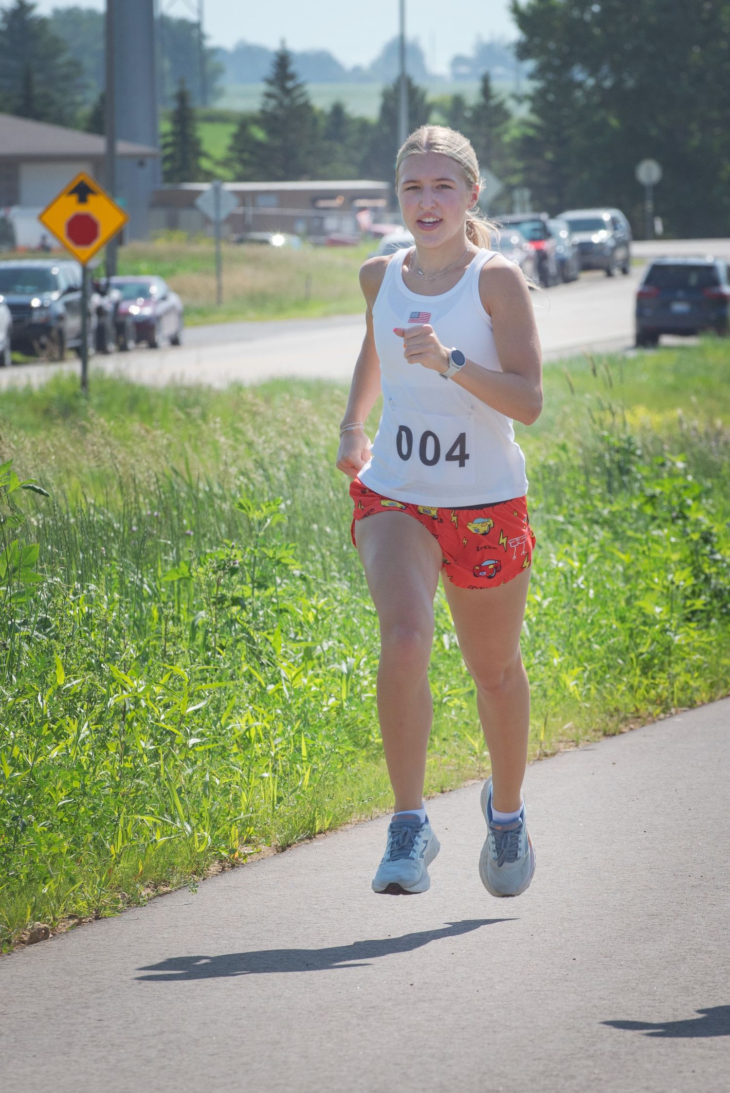 Young female runner wearing bib number 004 competing in an outdoor road race on a sunny summer day at Harmony MN 4th of July Celebration..