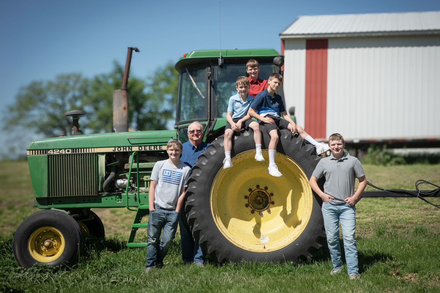 Family posing with a classic green John Deere tractor on a farm with a red barn.