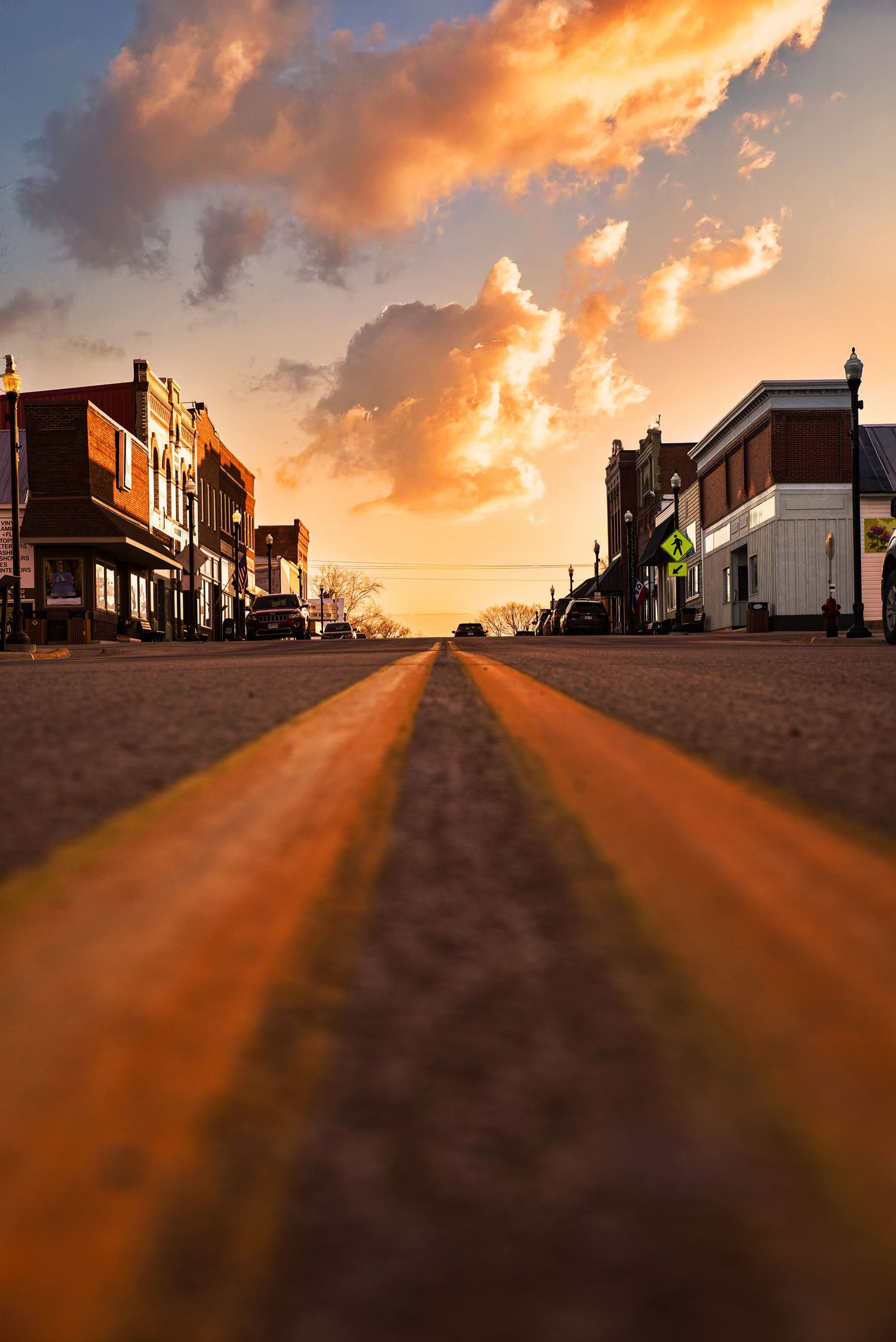 Low angle view of small town main street at dramatic golden sunset with glowing clouds.