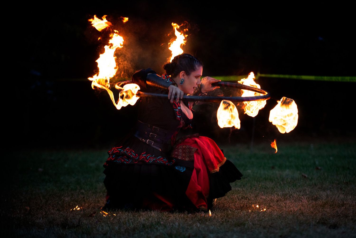 A fire dancer in a red and black costume spins flaming batons during a nighttime performance. Outside Monster 
Bash Harmony MN.