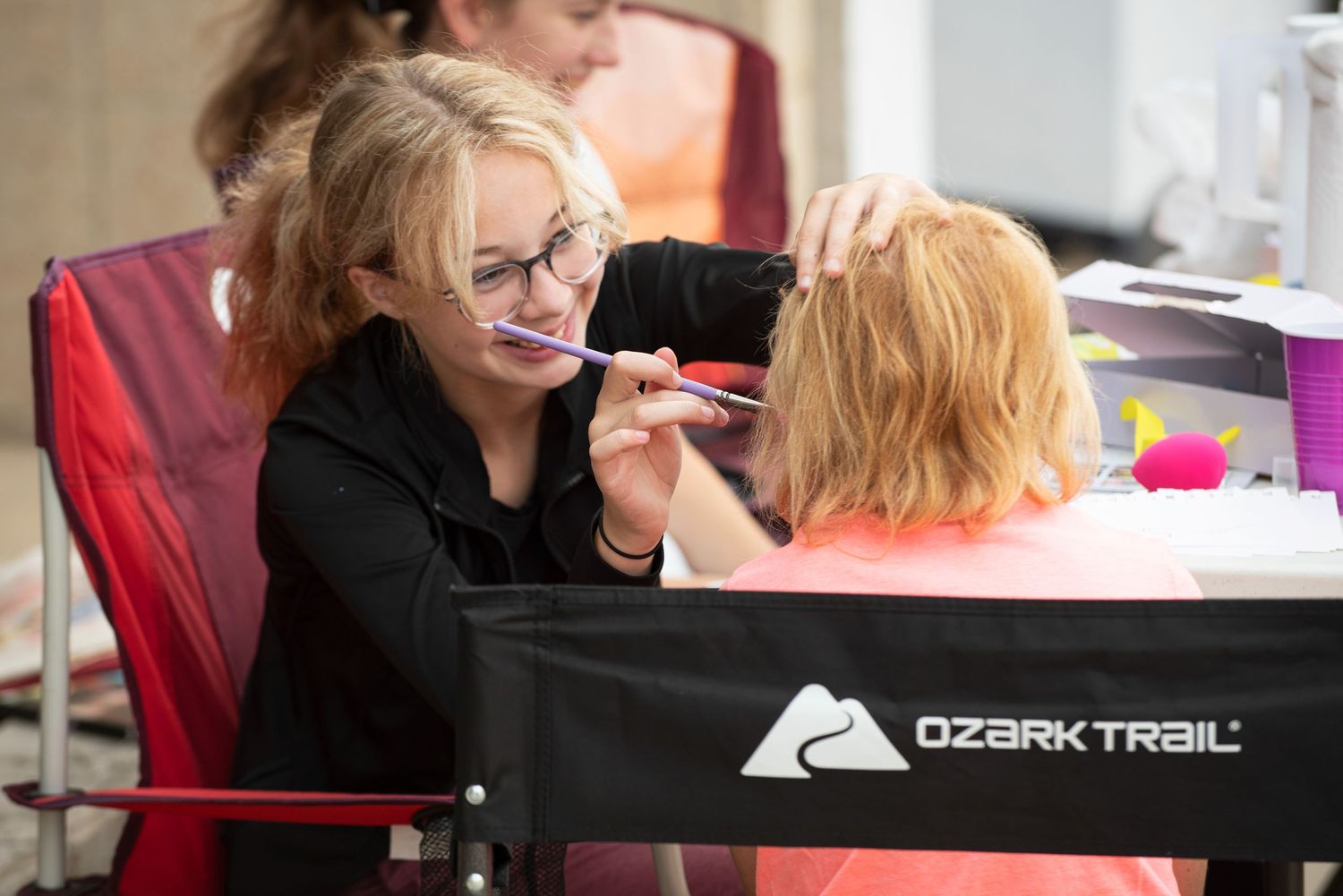 Woman carefully painting a young childs face at an outdoor festival event.