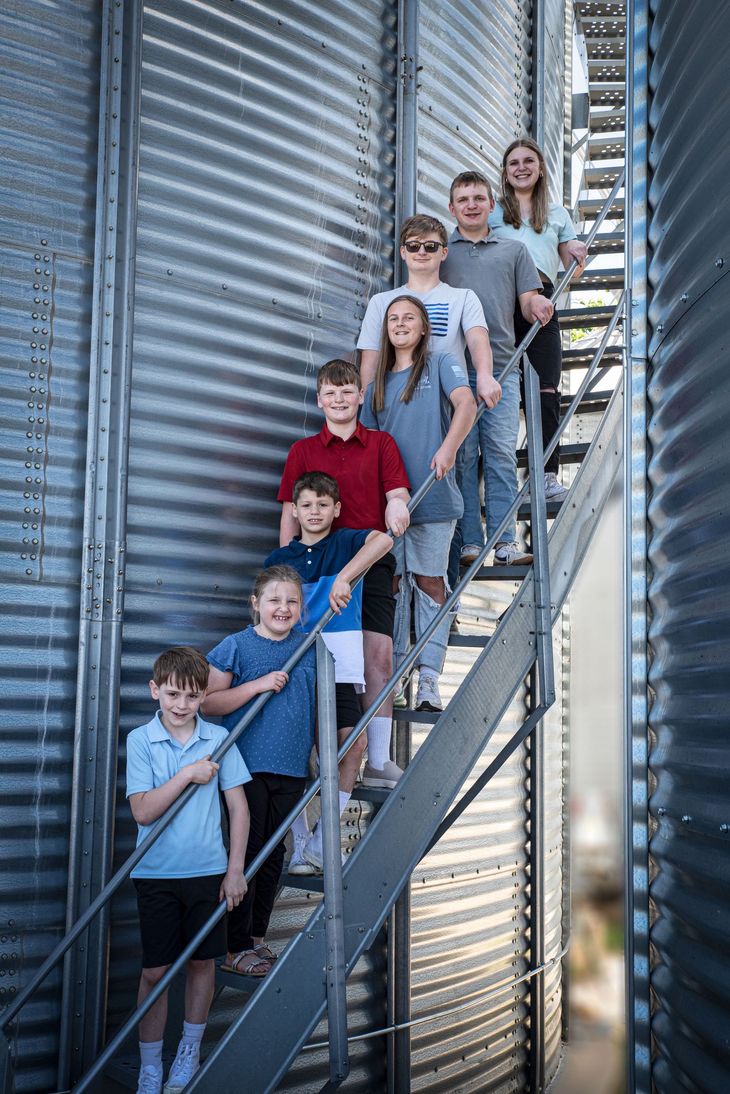 Group of eight children posing on metal grain bin stairs on a sunny day.