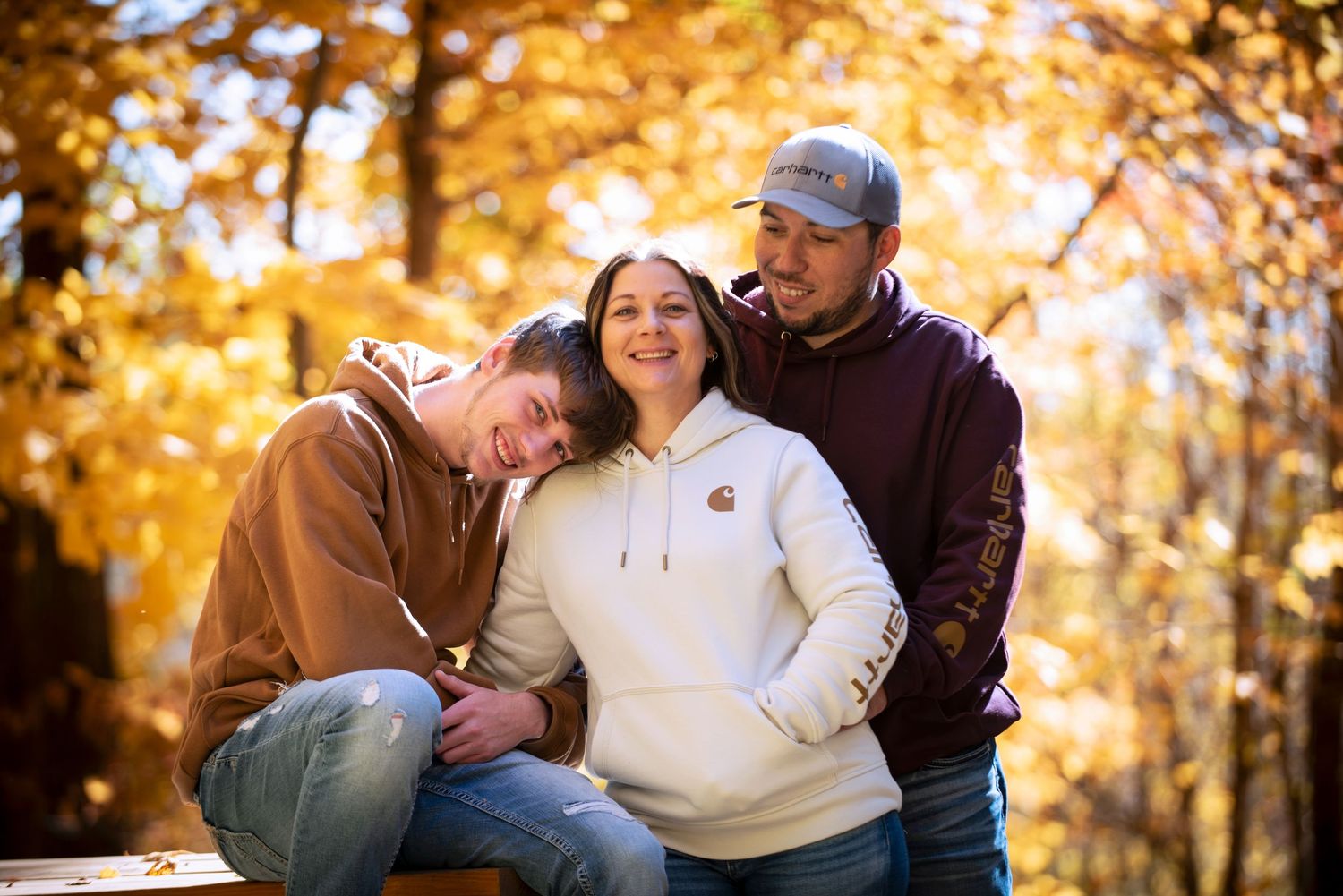 Three people sharing a warm embrace outdoors surrounded by vibrant autumn foliage.