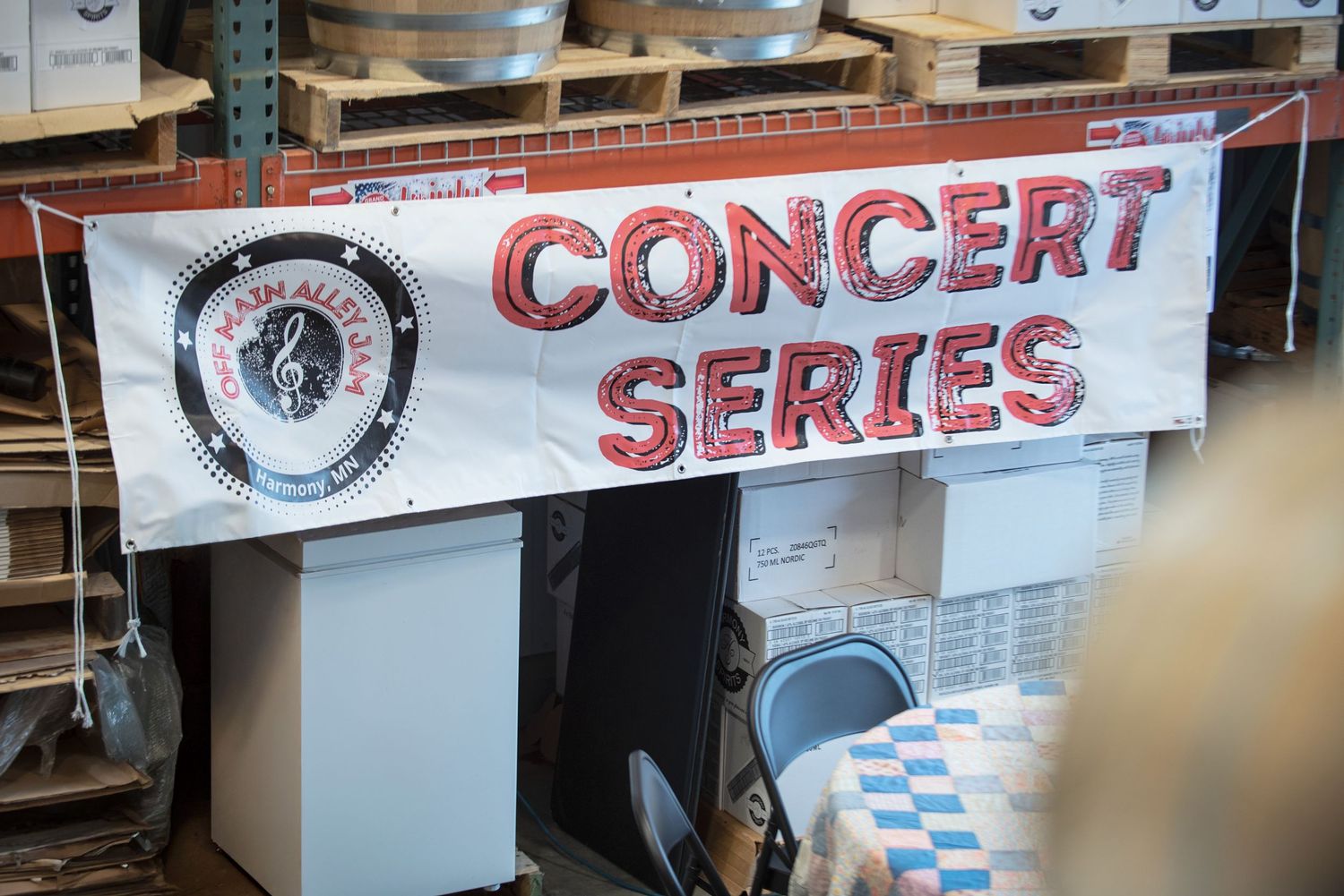 Concert Series banner sign displayed inside a warehouse venue with wooden pallets in the background at Harmony Spirits..
