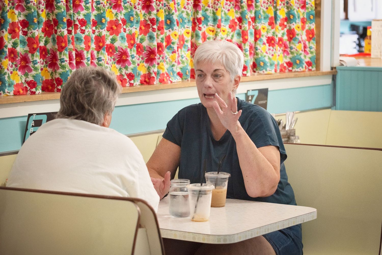 Two elderly women having a conversation over drinks at a retro diner table at Gabby Lou's.