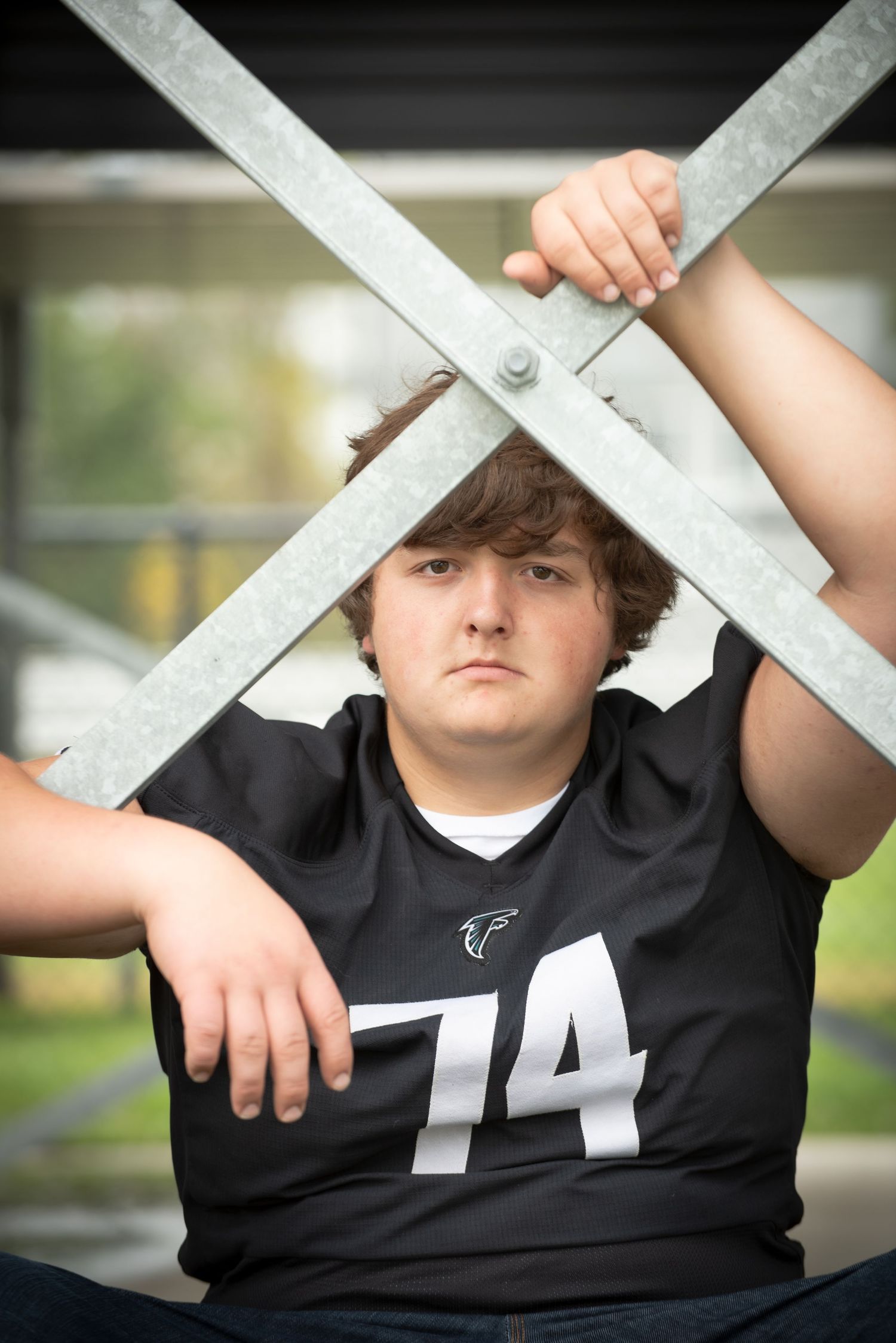 Teen football player number 74 posing with metal X structure outdoors.
