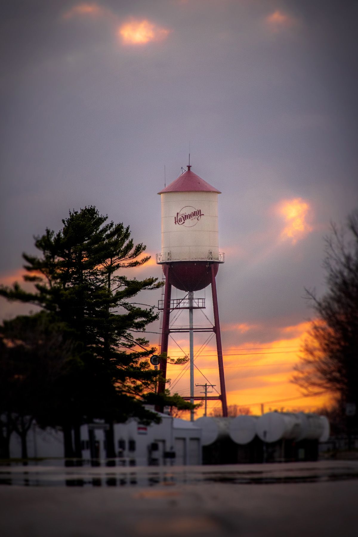 Vintage water tower at sunset with dramatic orange clouds and silhouetted trees.