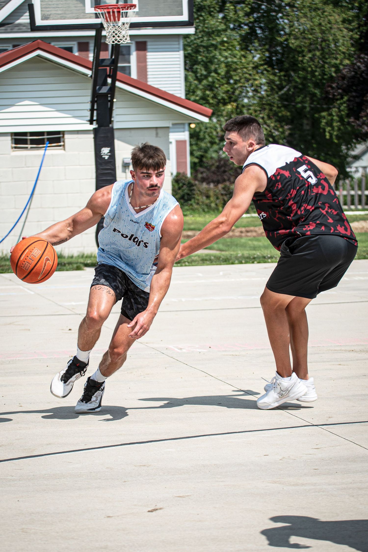 Young man dribbles basketball past defender on outdoor court during summer Rucker League game.