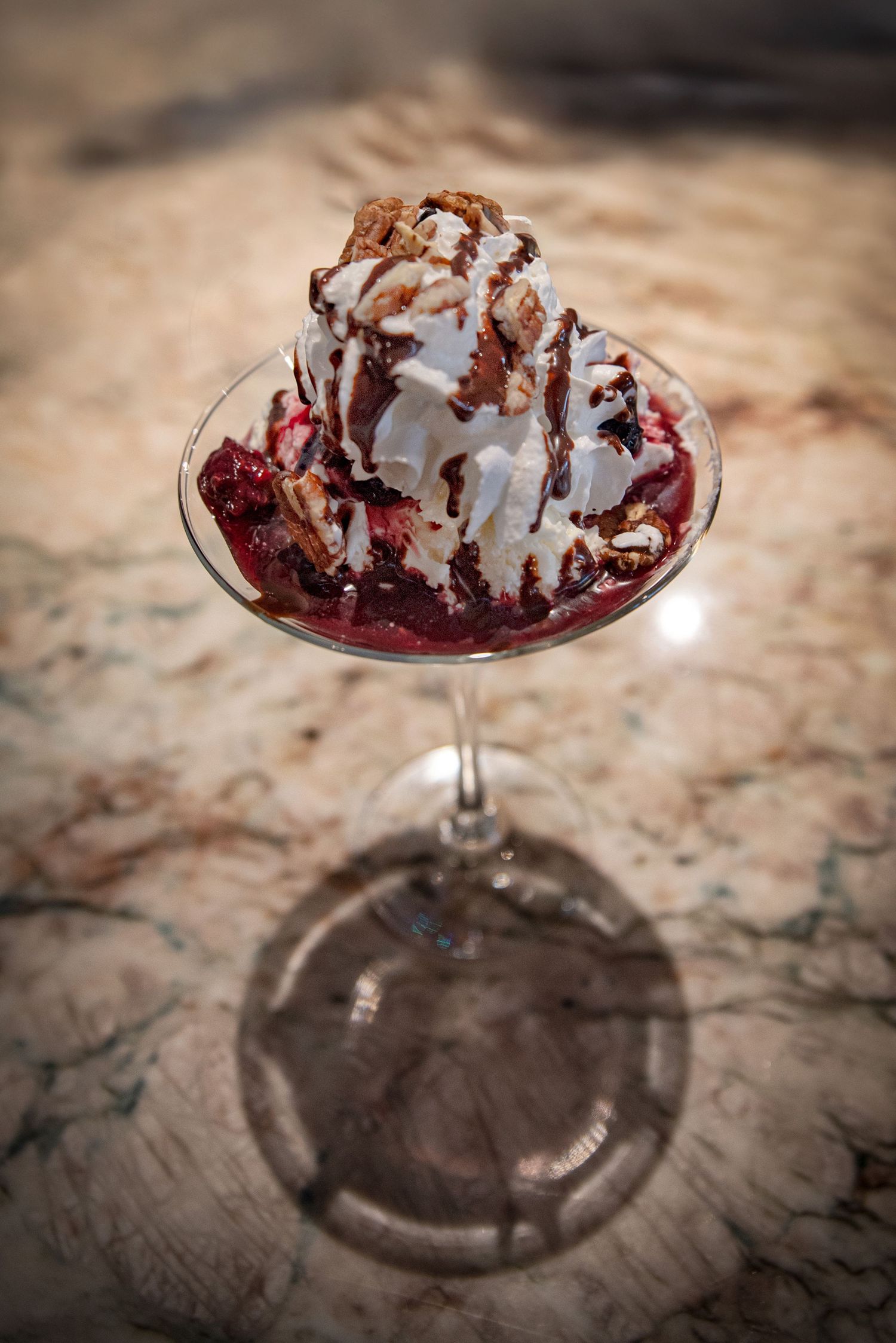 Ice cream sundae with whipped cream and chocolate sauce in a glass on a marble surface at Estelle's Eatery.