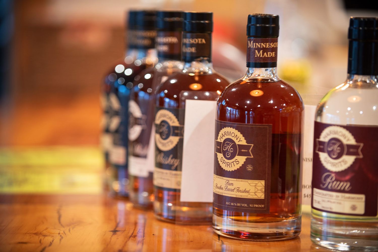 Row of Minnesota Made whiskey and rum bottles displayed on a wooden counter at a distillery at Harmony Spirits..