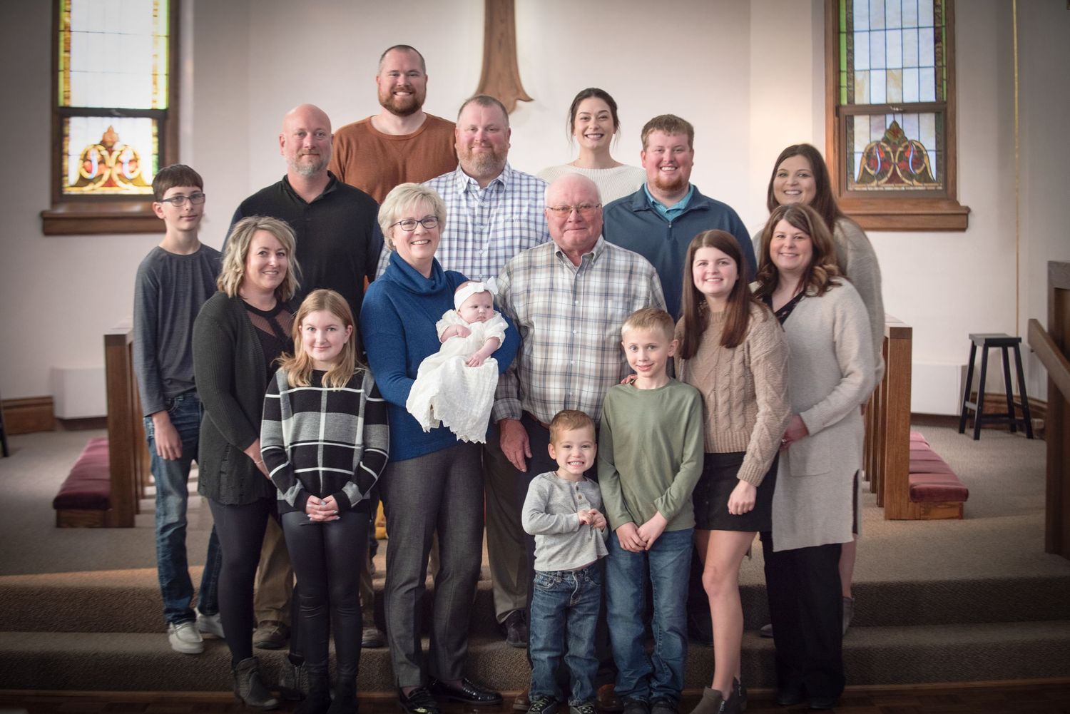 Multi-generational family portrait taken inside a church, featuring adults and children smiling together near wooden pews.