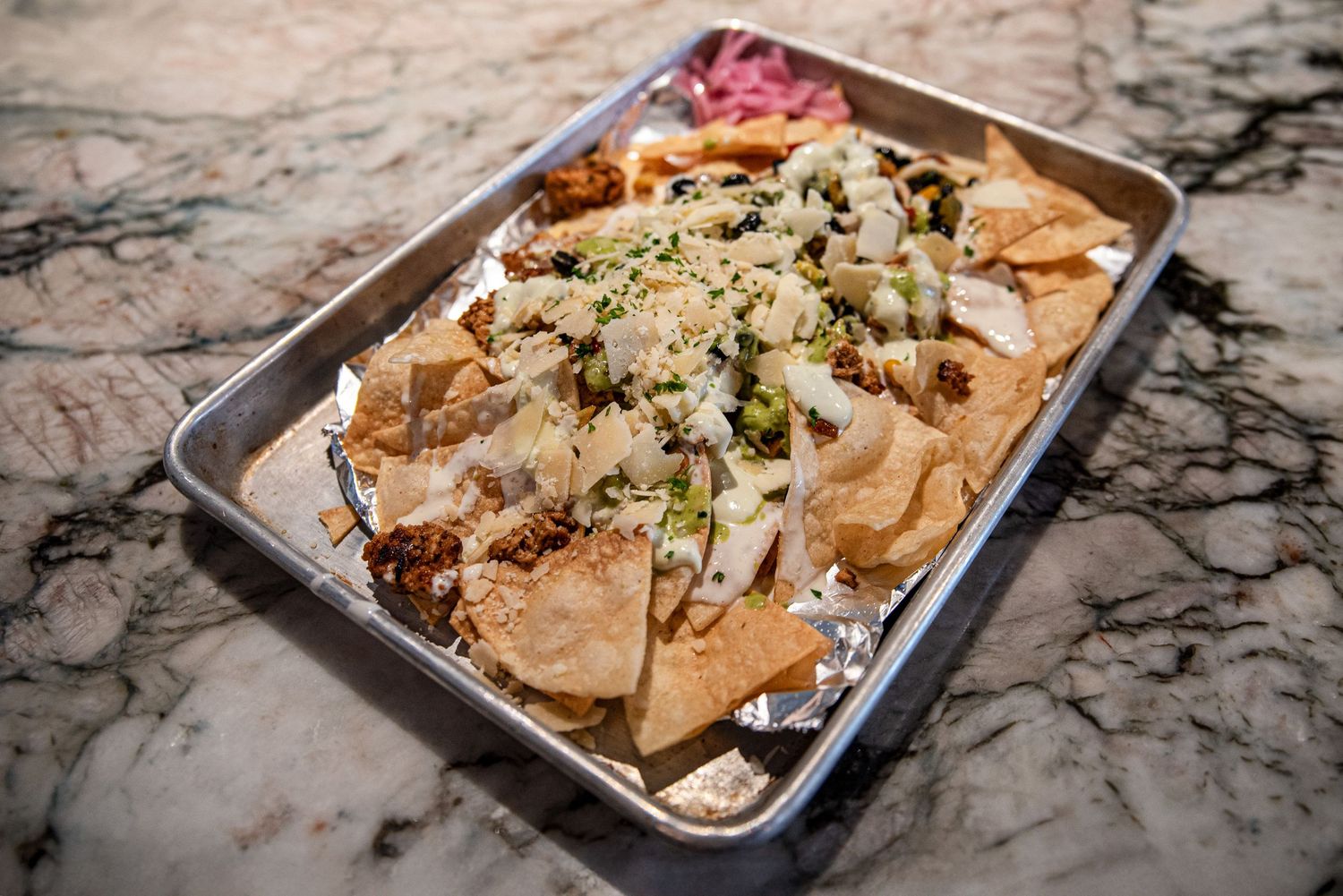 Loaded nachos topped with cheese, green onions, and toppings served on a foil-lined tray at Estelle's Eatery.