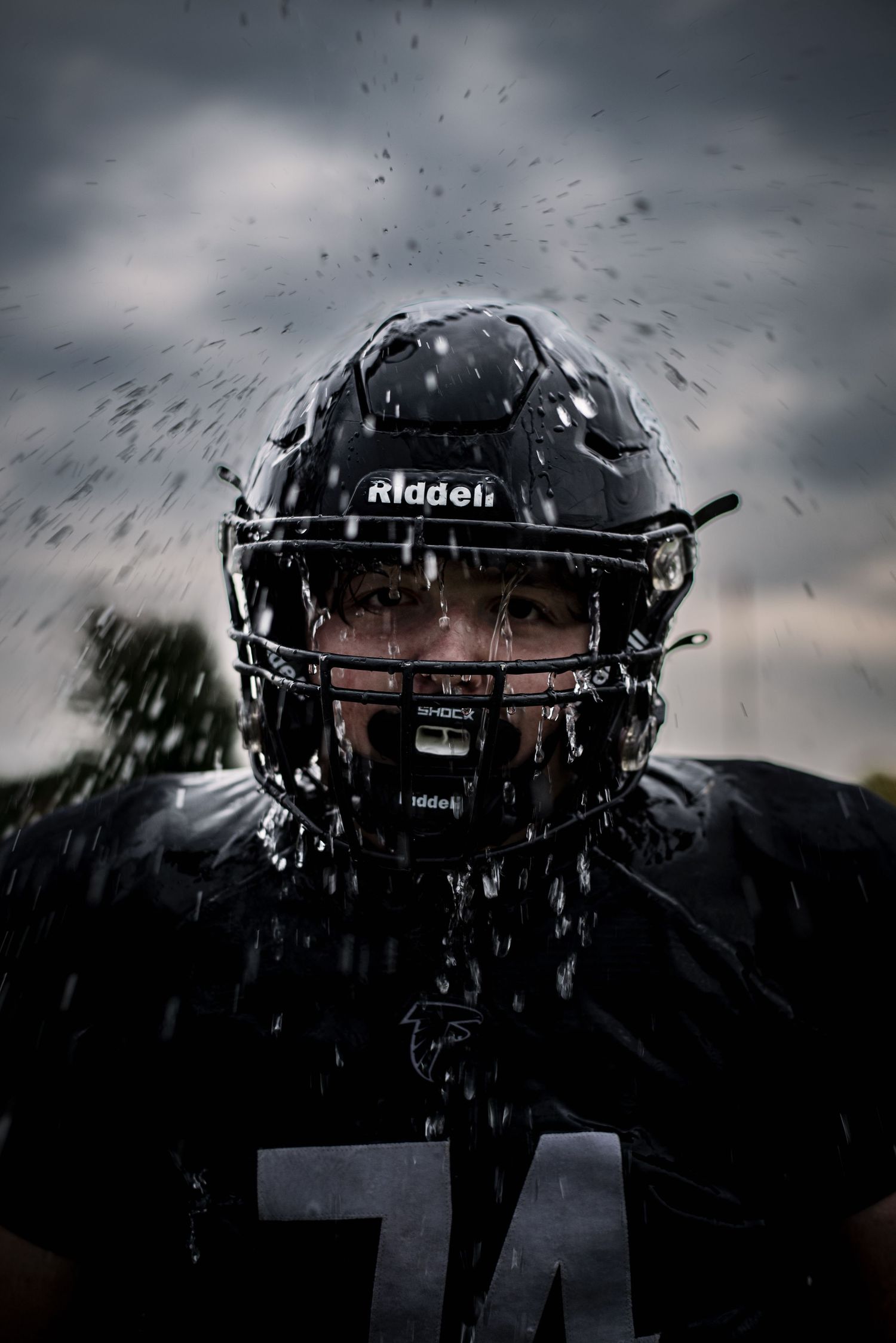Fillmore Central Football player in black Riddell helmet and jersey with water splashing dramatically.
