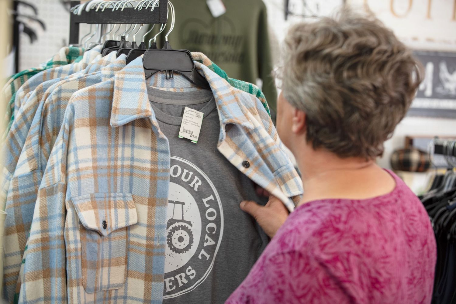 Woman browsing plaid flannel shirts on a clothing rack at a retail store in front of Farm Charm.