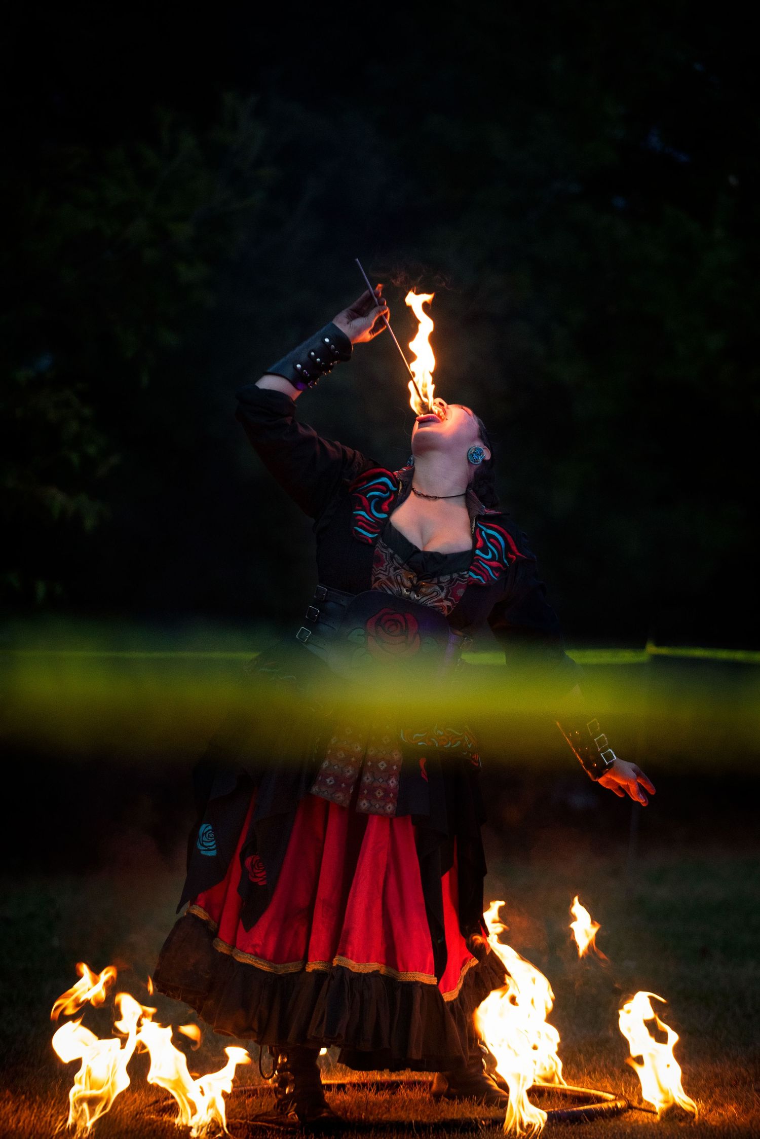 A fire performer in a red and black costume eats fire during a nighttime outdoor show.Outside Monster 
Bash Harmony MN.