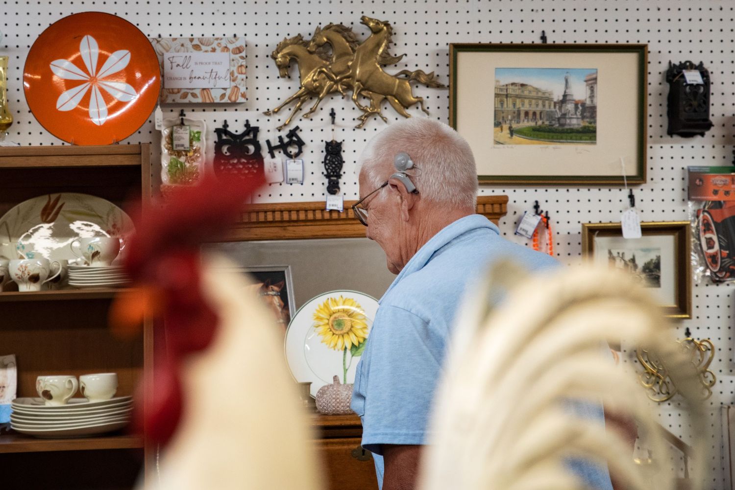 Elderly man browses antique shop filled with decorative roosters, plates, and vintage wall art at  Bee Balm Boutique.