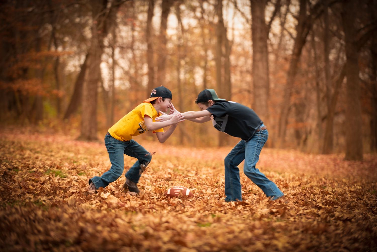 Two boys playing football in autumn leaves in a forest.