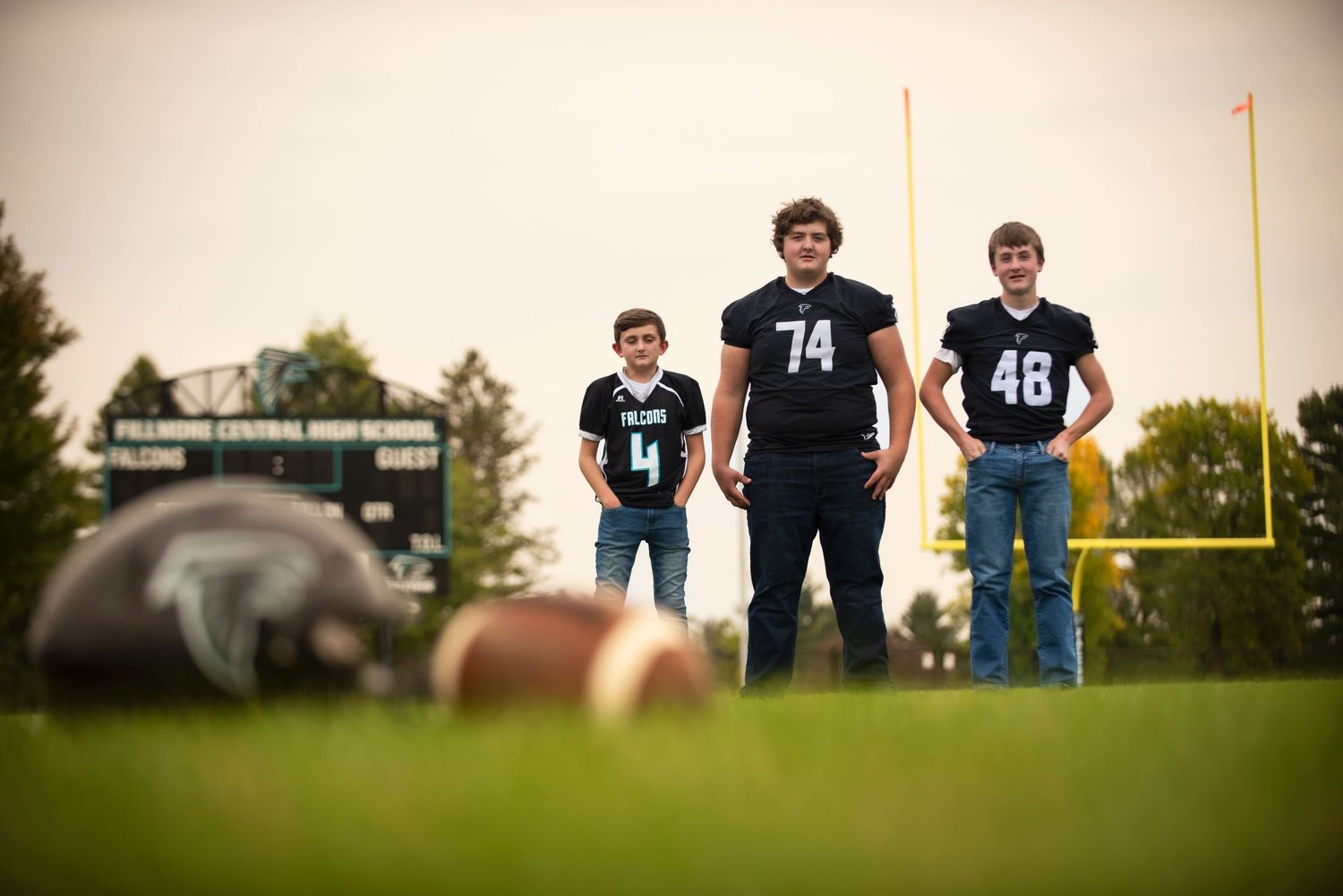 Three Fillmore Central brothers in football jerseys posing on a green field with goalposts in background.