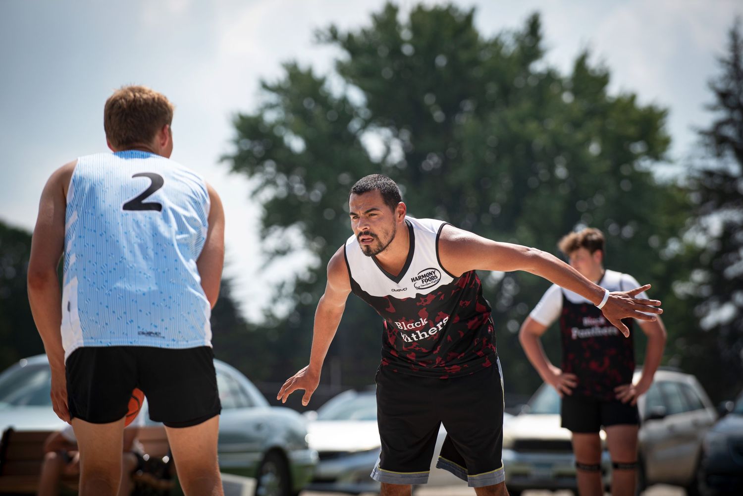 Basketball player in white jersey number 2 faces off against defender in outdoor Rucker League game.