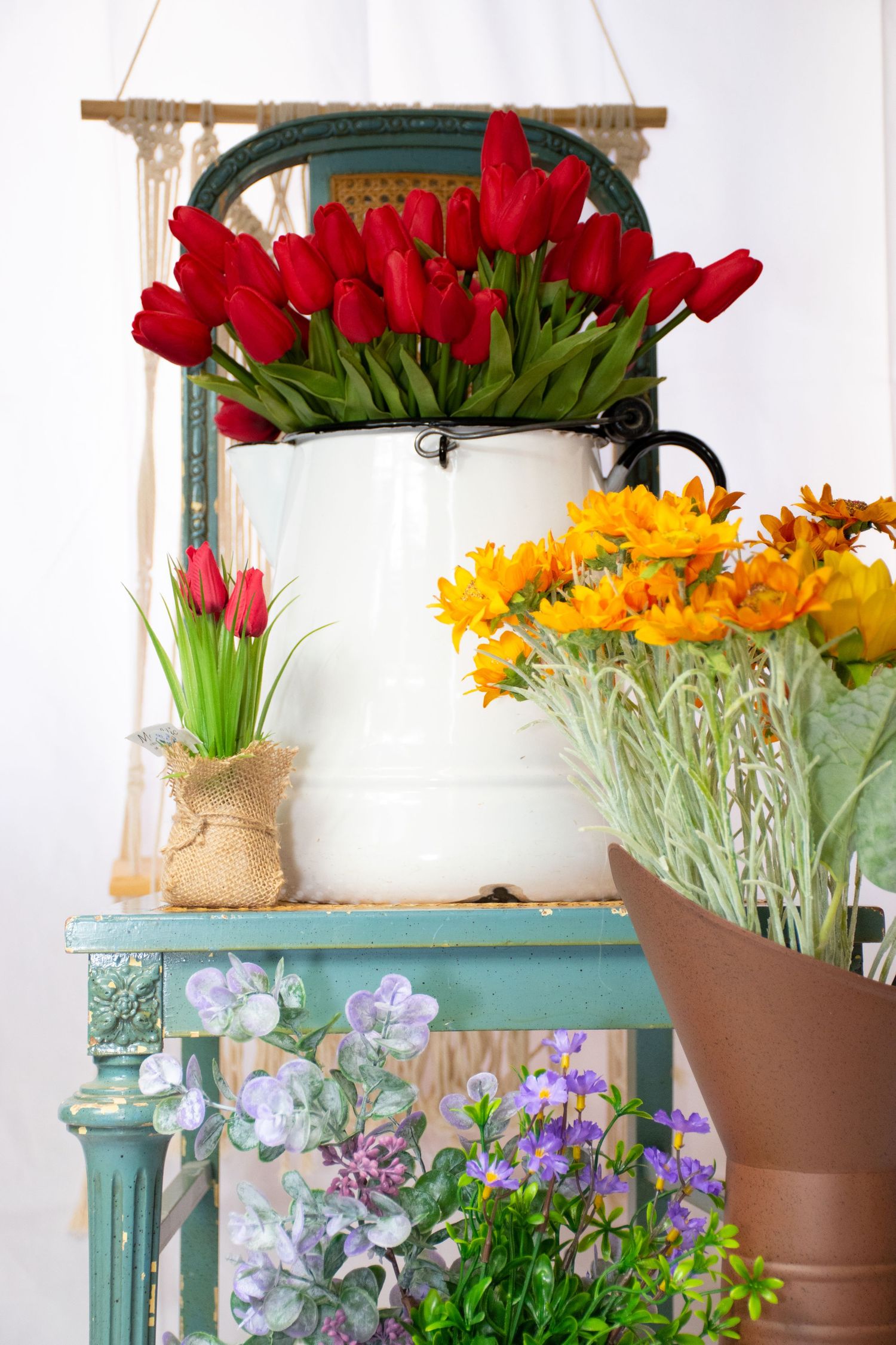 Vibrant red tulips and yellow flowers arranged in white enamel pot on teal vintage table at Bee Balm Boutique.