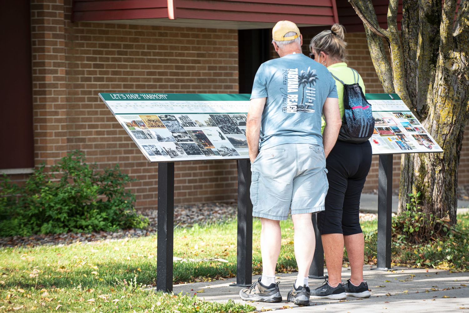 Two people reading an outdoor historical information display board outside a brick building at Harmony MN Tourist Center..