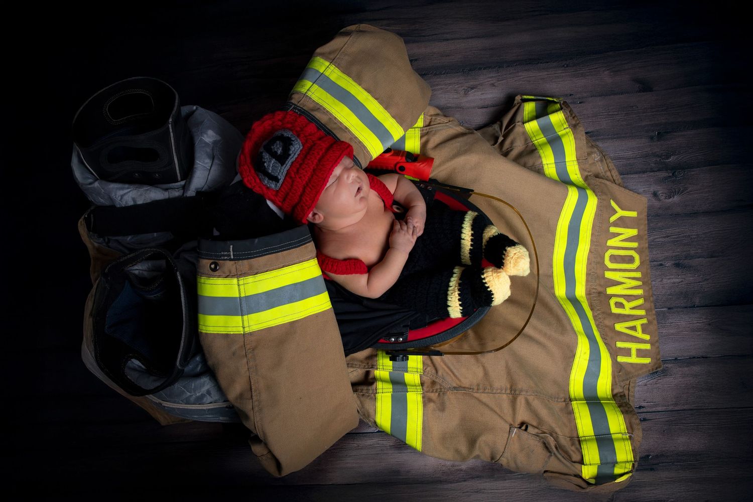 Newborn baby sleeps peacefully on a firefighter jacket and helmet in a tribute newborn photo.