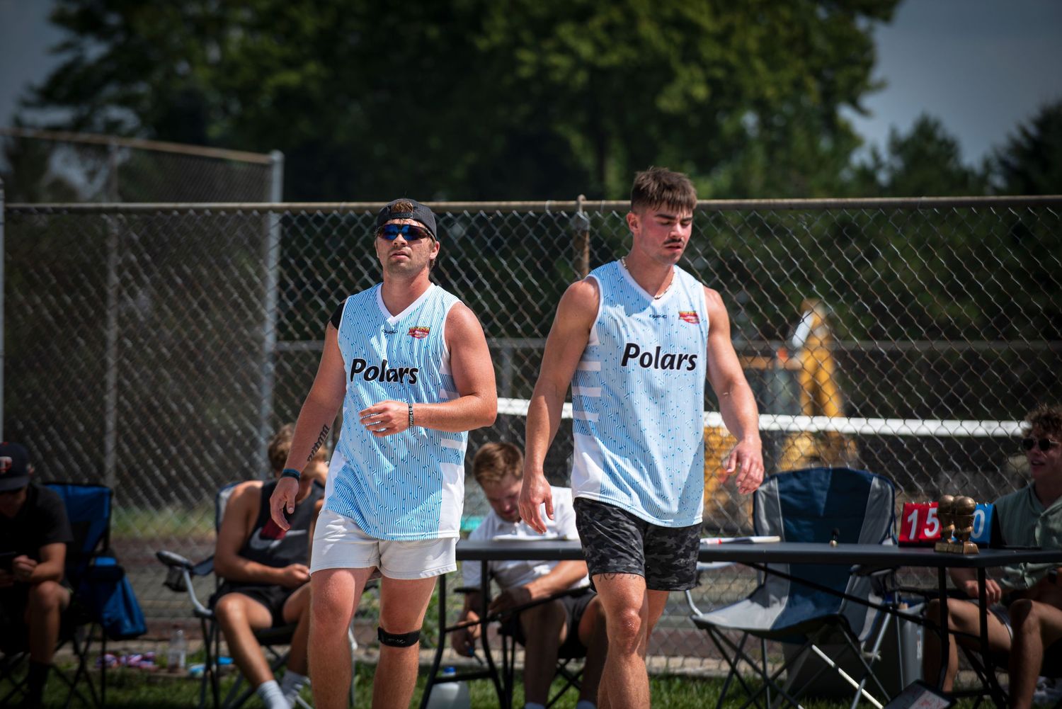 Two male basketball players walk on an outdoor court during a sunny summer Rucker League tournament.