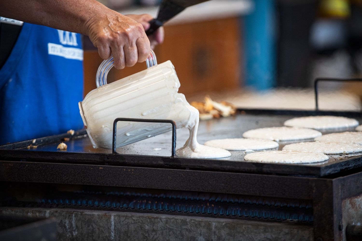 Pancake batter being poured onto a large flat-top griddle at an outdoor community breakfast. 4th of July Celebration in Harmony MN.