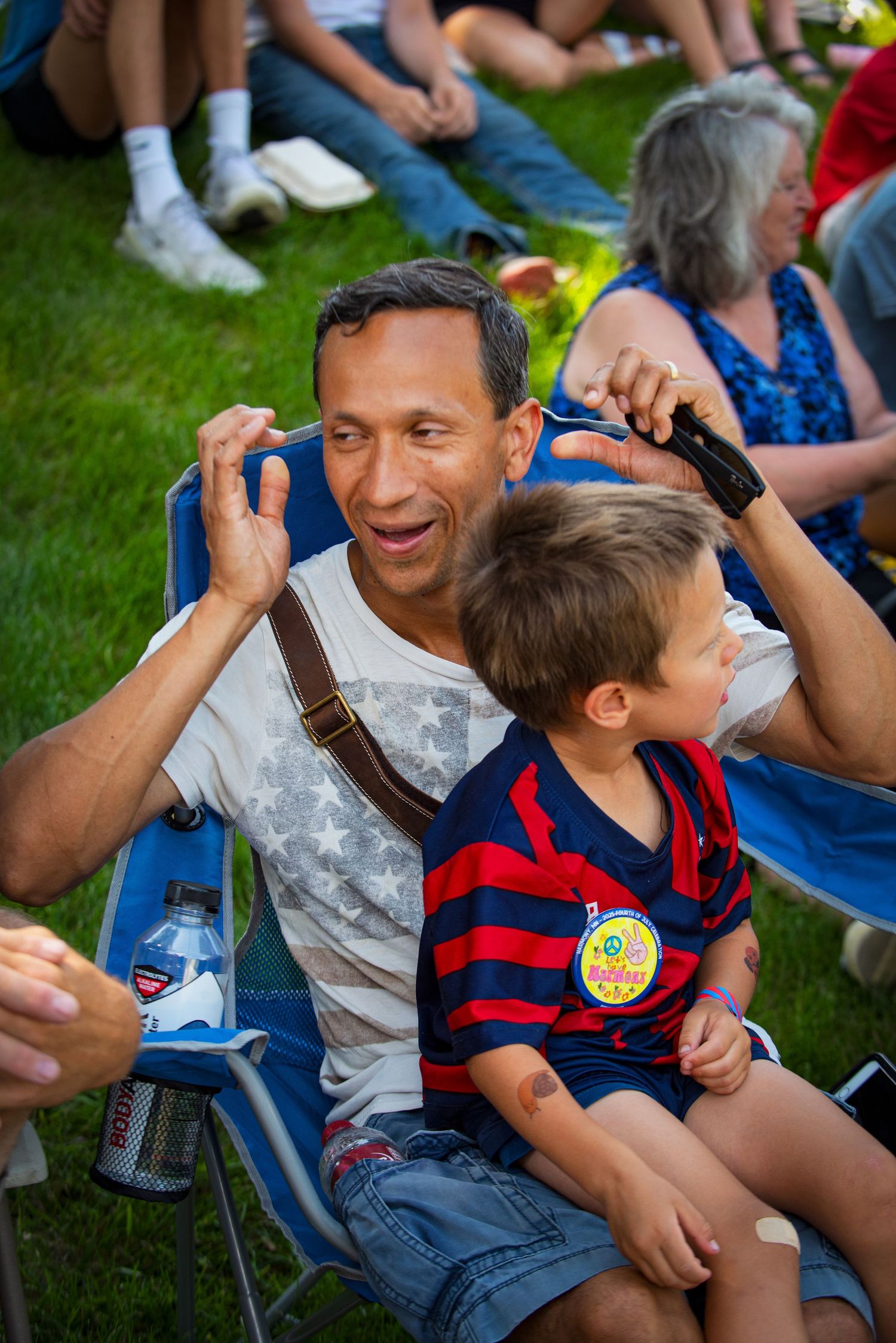 A smiling man holds a young boy on his lap while enjoying an outdoor summer festival. At Harmony MN 4th of July Celebration.