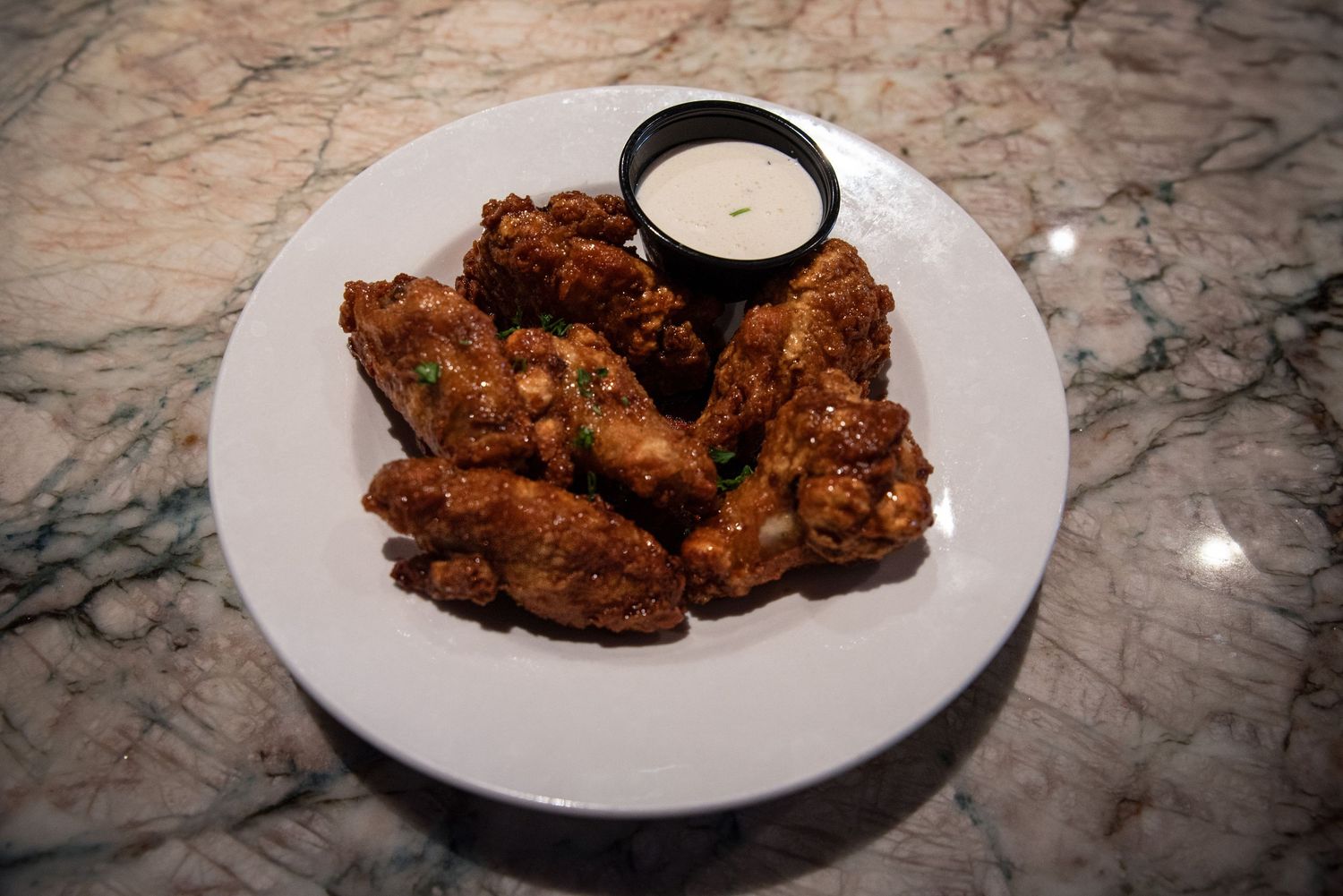Crispy fried chicken wings served with ranch dipping sauce on a white plate at Estelle's Eatery.