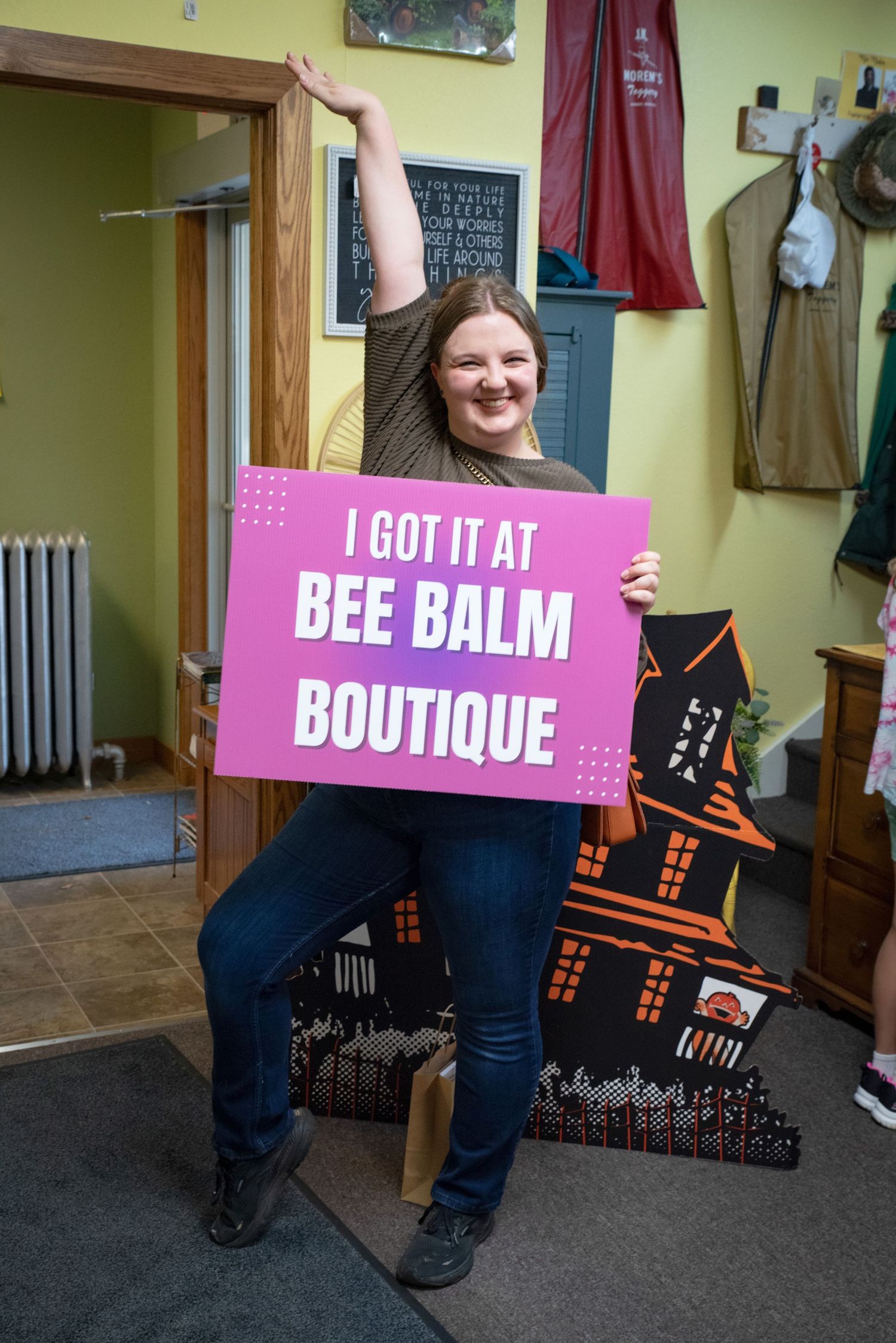 Happy woman poses with a Bee Balm Boutique sign inside a charming boutique store.