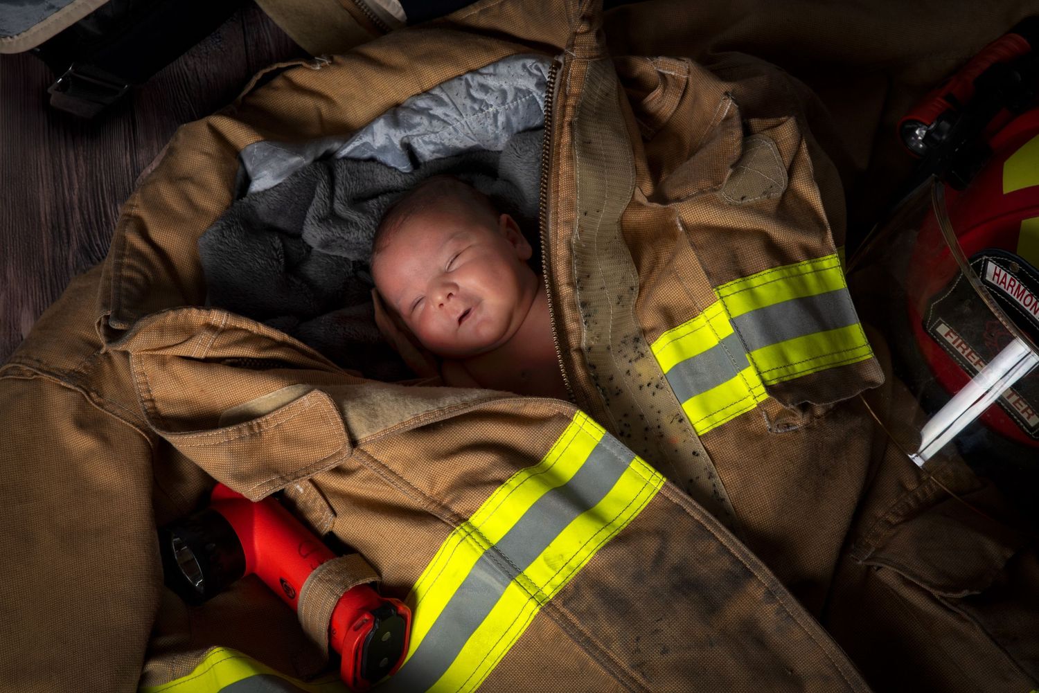 Newborn baby nestled inside an open firefighter turnout gear jacket surrounded by fire equipment.