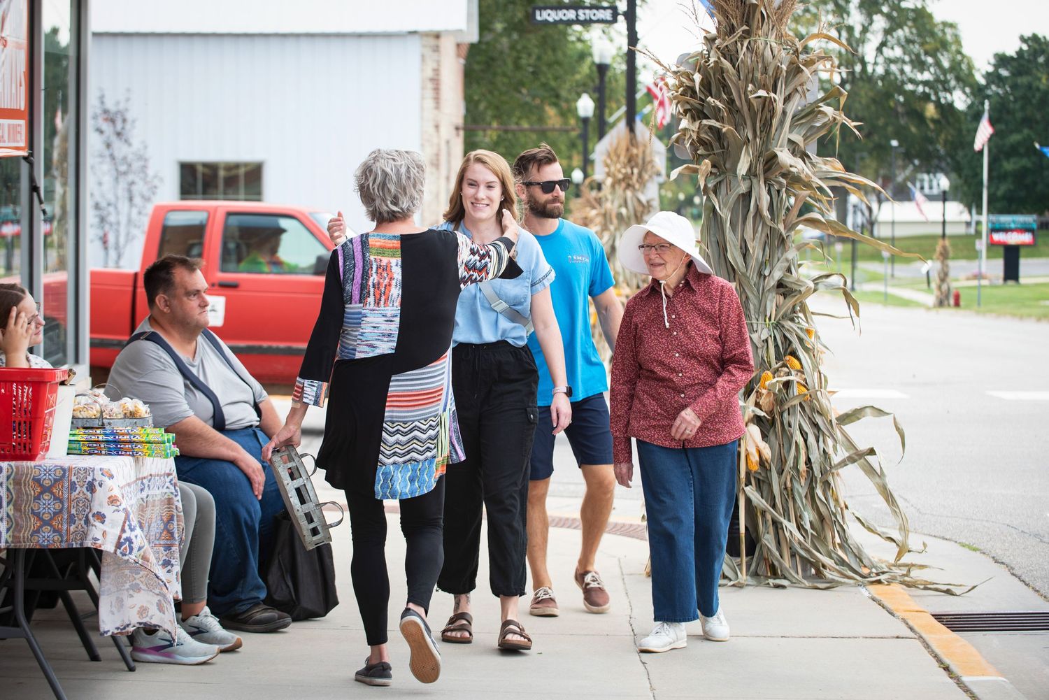 People walking along a small town sidewalk during an outdoor community festival event.