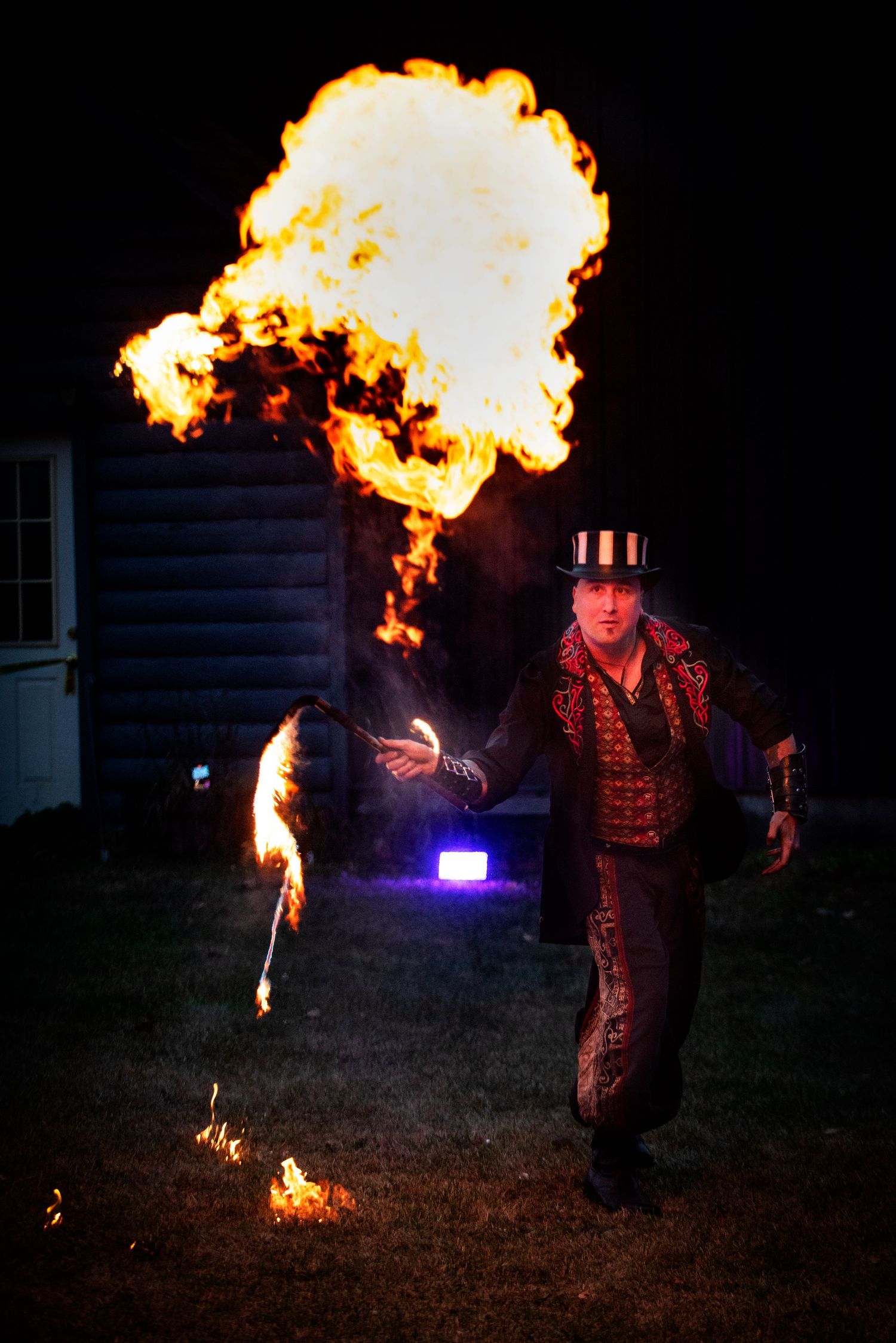 A male fire breather in a top hat shoots a large fireball during an outdoor nighttime performance. Outside Monster 
Bash Harmony MN.