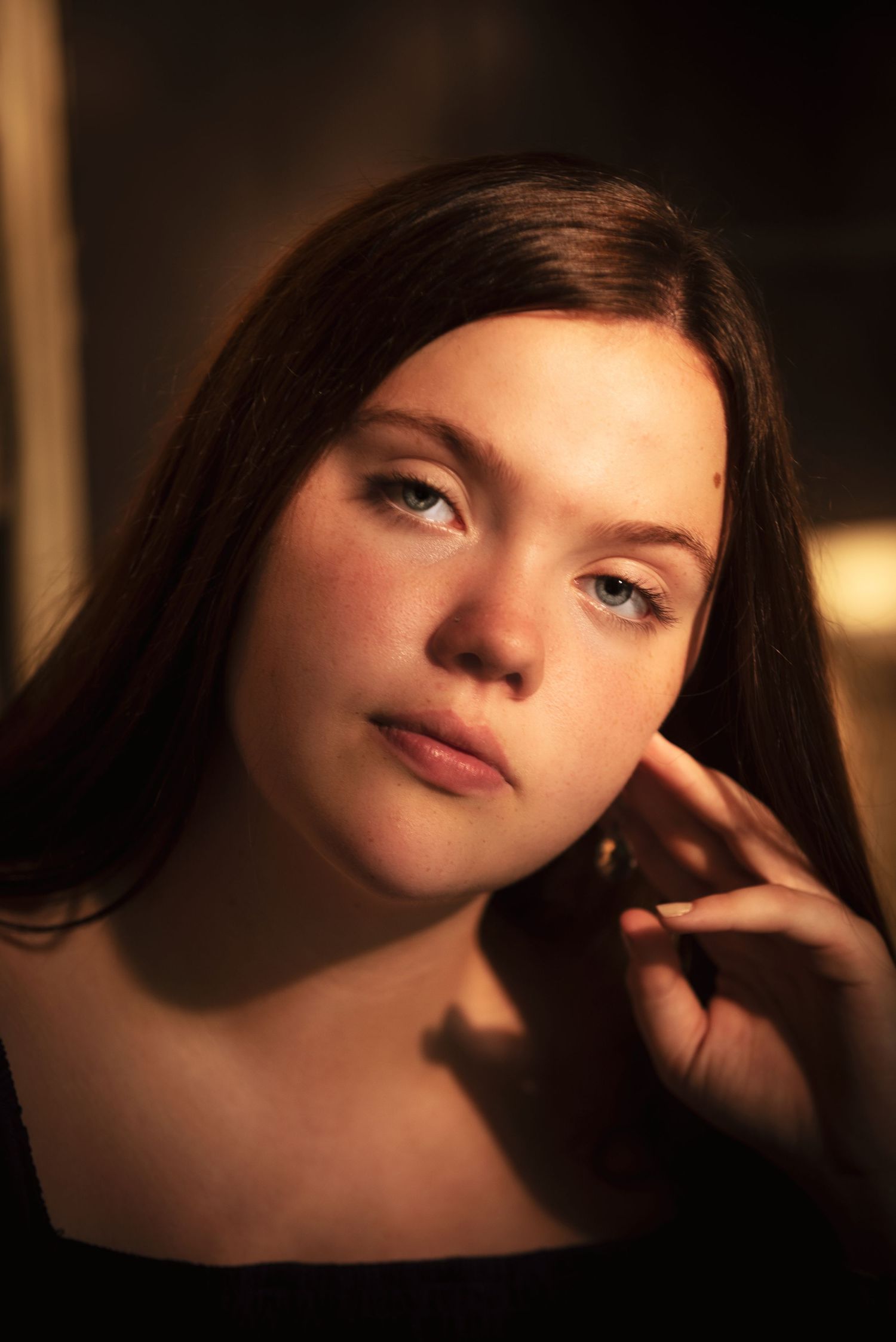 Close-up portrait of a young brunette woman in warm golden light touching her face.