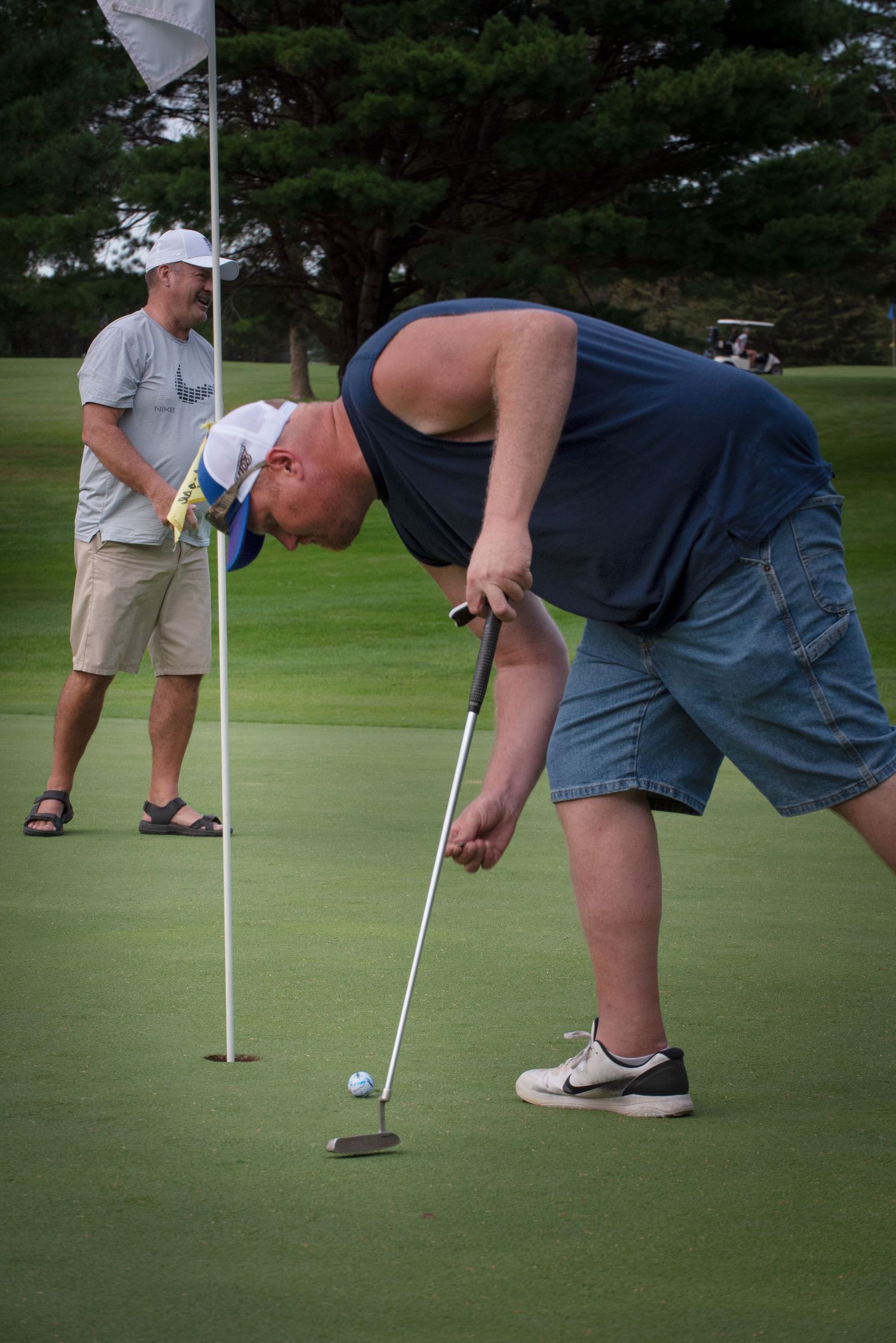 Golfer putting on a green while another player watches from behind the flag.
