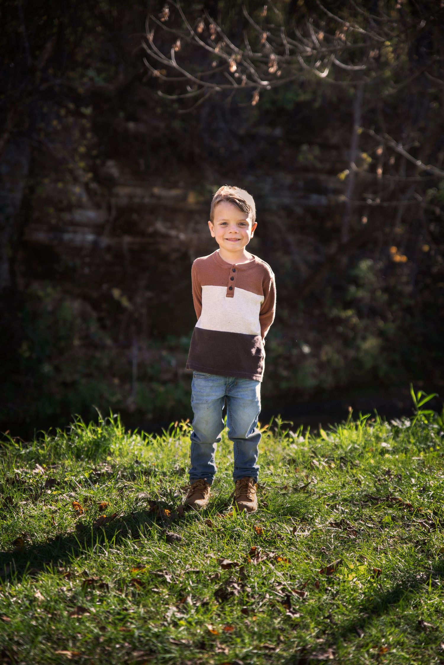 Cheerful young boy in colorful striped shirt standing on green grass in sunny park.